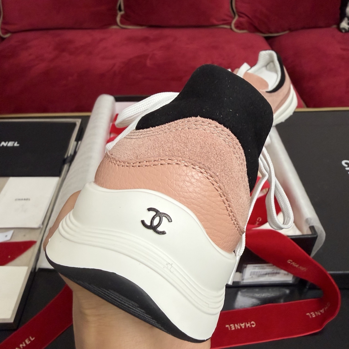 A pair of pink and black Chanel sneakers with white laces sitting on a luxury gift box with red ribbons - Hình 8