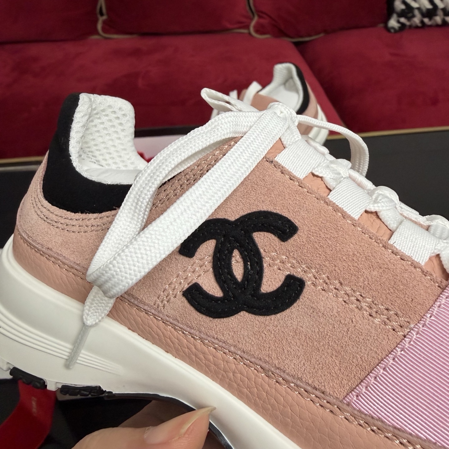 A pair of pink and black Chanel sneakers with white laces sitting on a luxury gift box with red ribbons - Hình 7