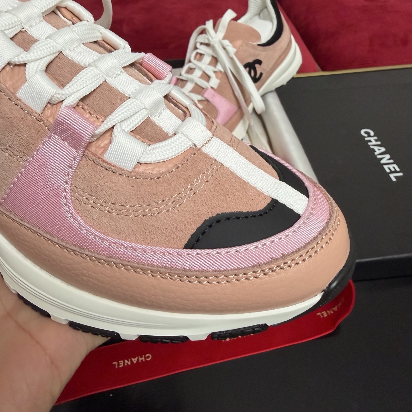 A pair of pink and black Chanel sneakers with white laces sitting on a luxury gift box with red ribbons - Hình 6