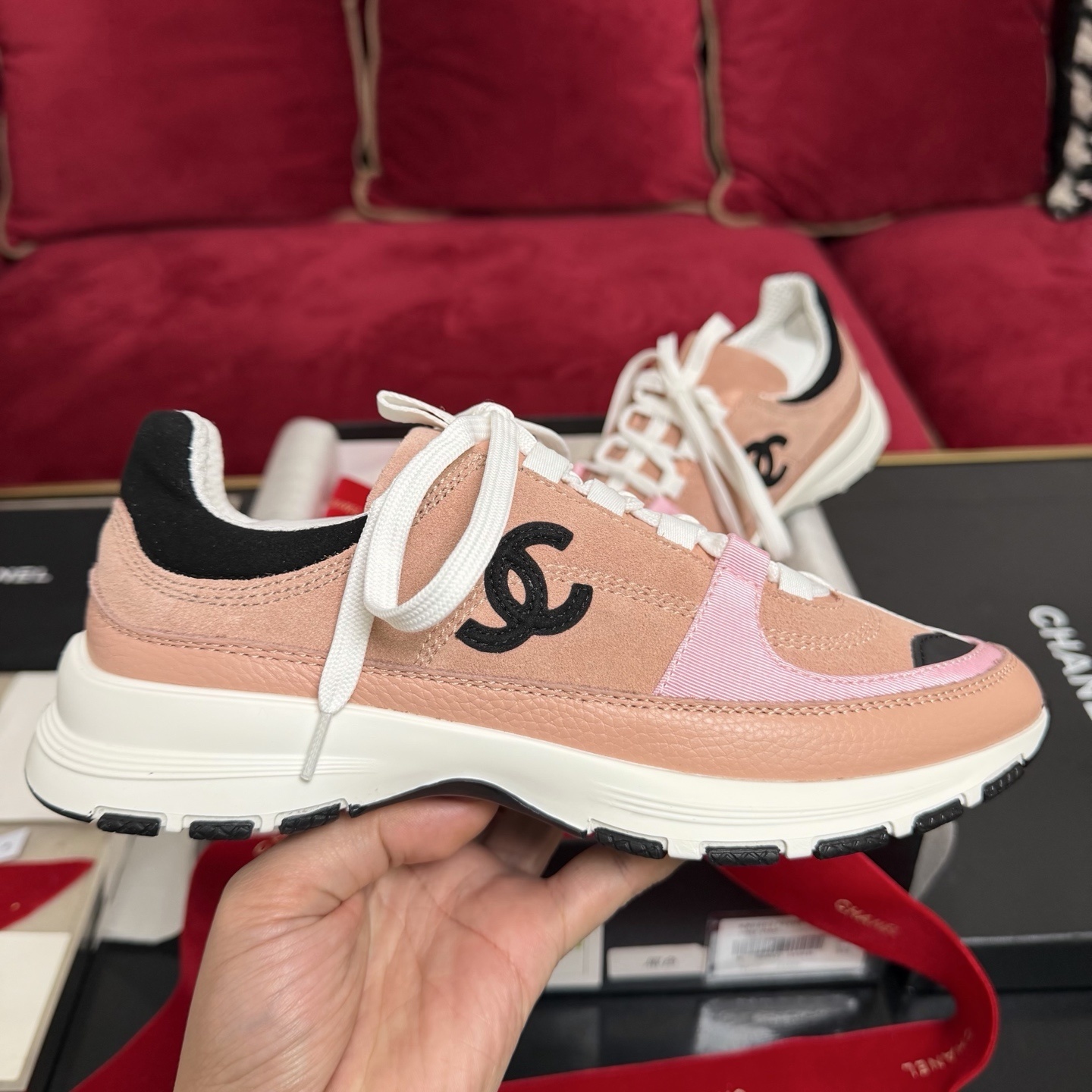 A pair of pink and black Chanel sneakers with white laces sitting on a luxury gift box with red ribbons - Hình 5