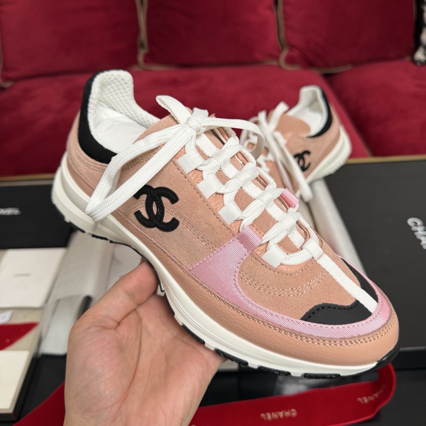 A pair of pink and black Chanel sneakers with white laces sitting on a luxury gift box with red ribbons - Hình 4