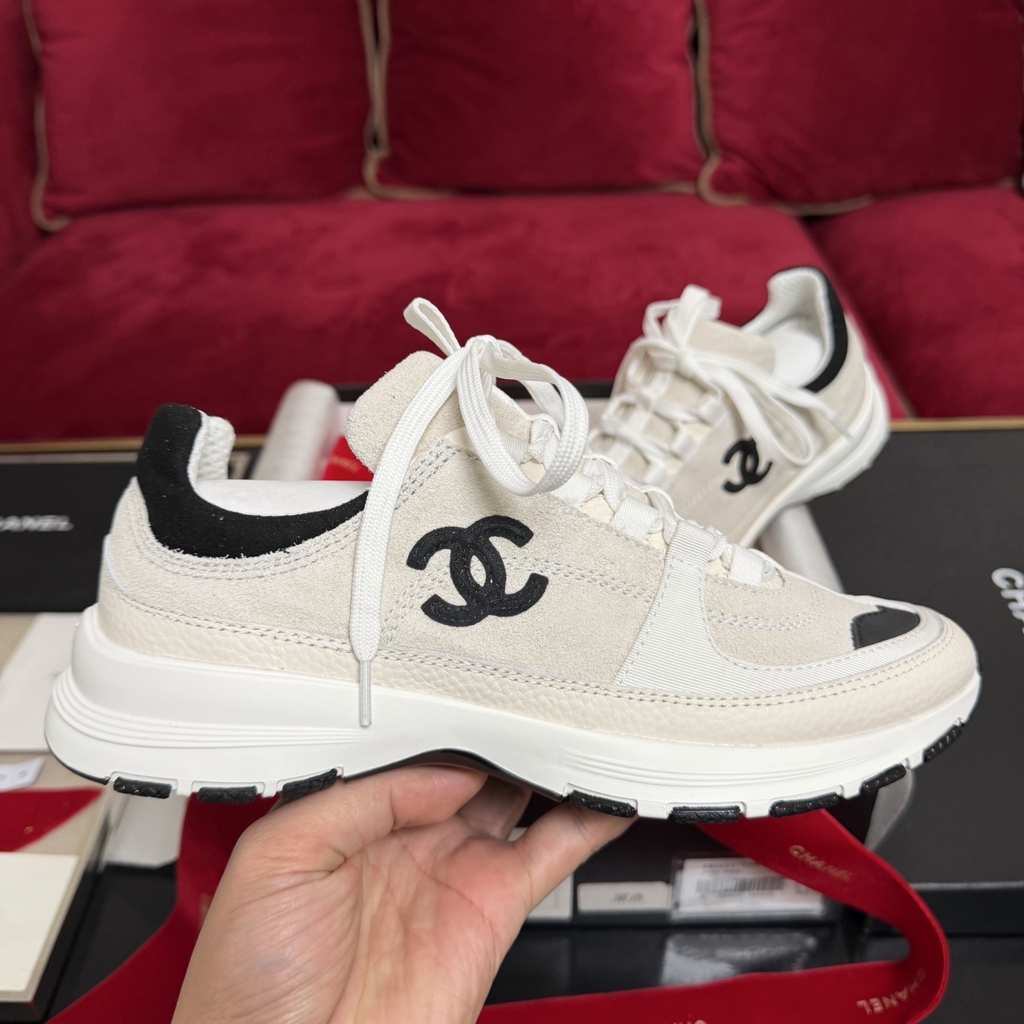 Authentic Chanel sneakers in cream and black featuring the iconic CC logo, presented in a luxury box with red ribbons. - Hình 5
