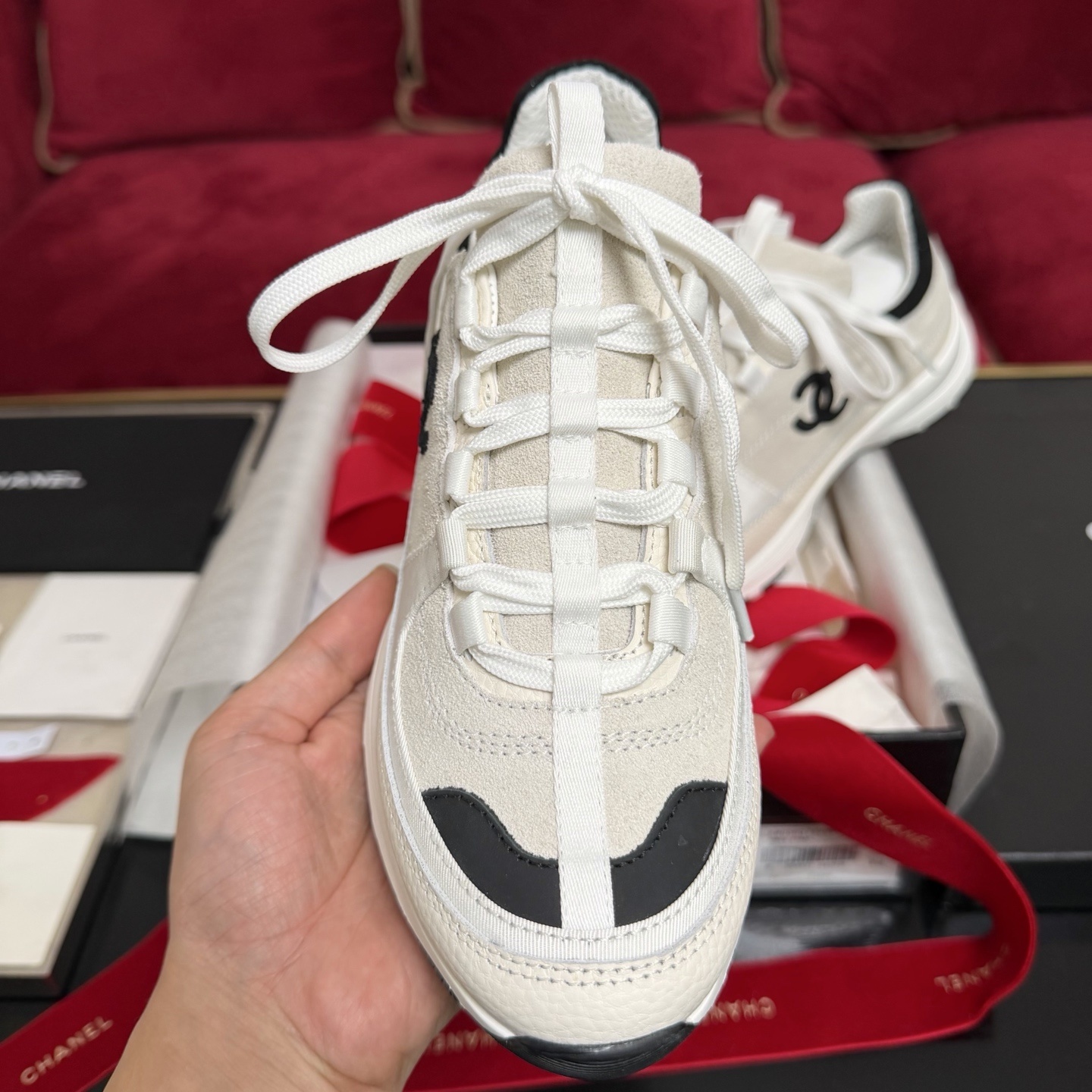Authentic Chanel sneakers in cream and black featuring the iconic CC logo, presented in a luxury box with red ribbons. - Hình 3