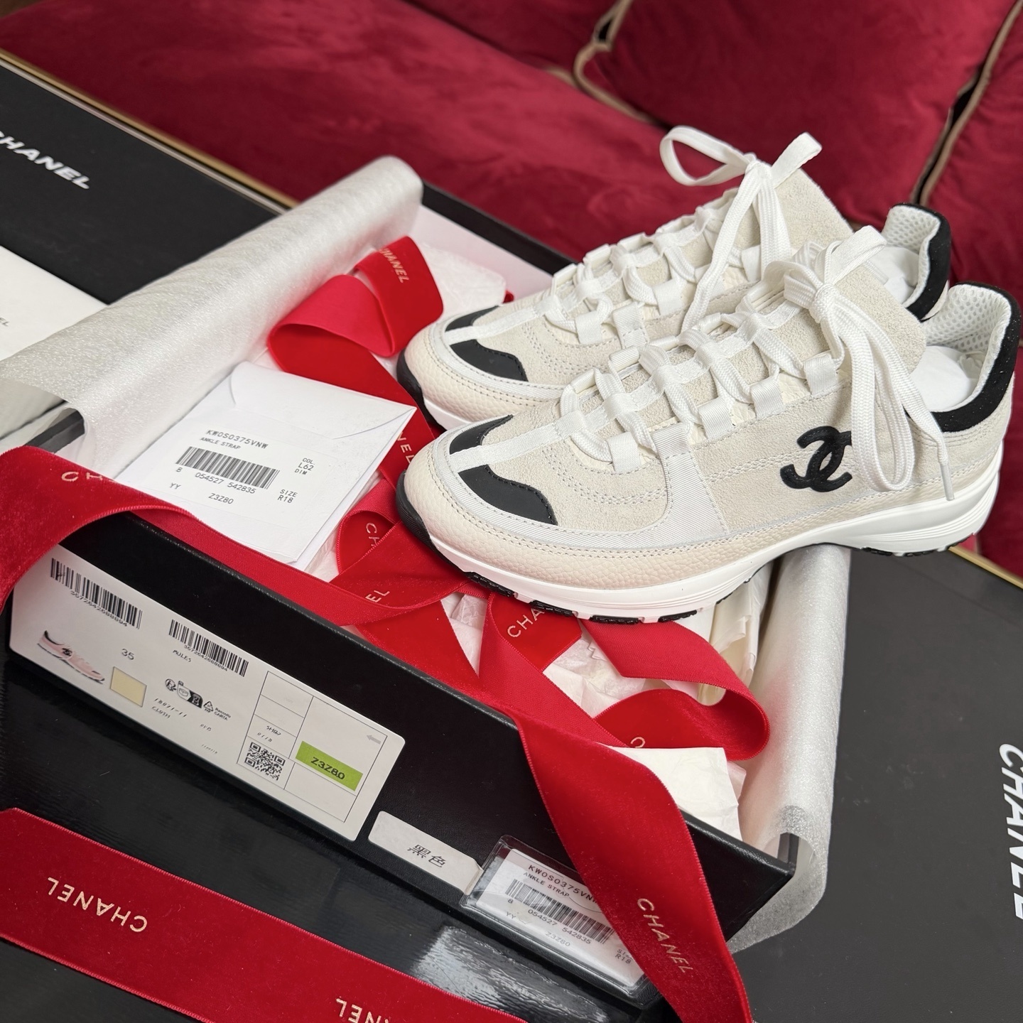 Authentic Chanel sneakers in cream and black featuring the iconic CC logo, presented in a luxury box with red ribbons. - Hình 2