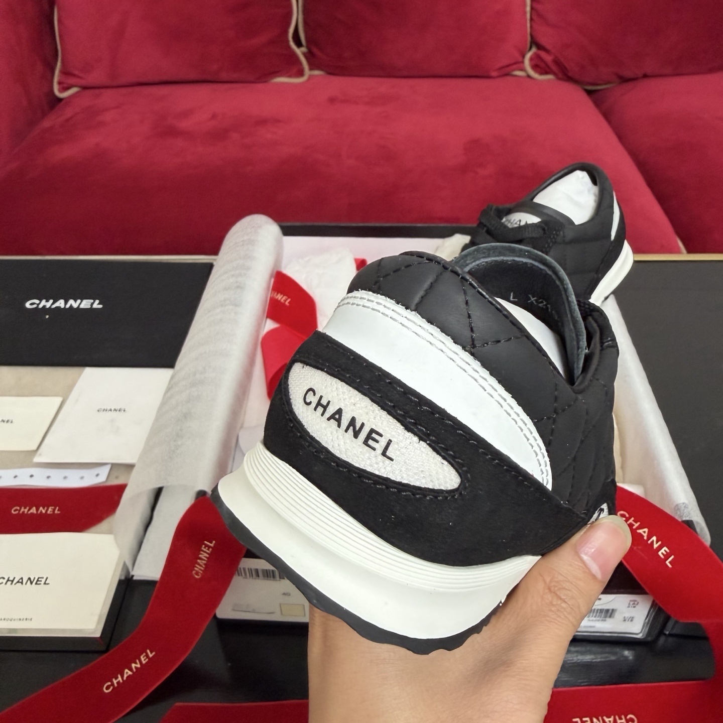 A pair of Chanel black quilted leather sneakers with white soles presented in luxury packaging with red ribbons - Hình 8