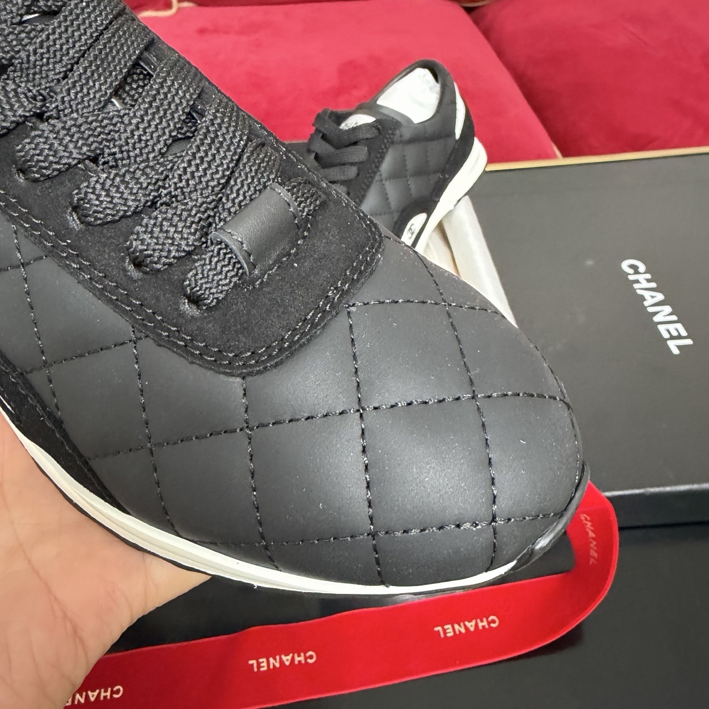 A pair of Chanel black quilted leather sneakers with white soles presented in luxury packaging with red ribbons - Hình 6