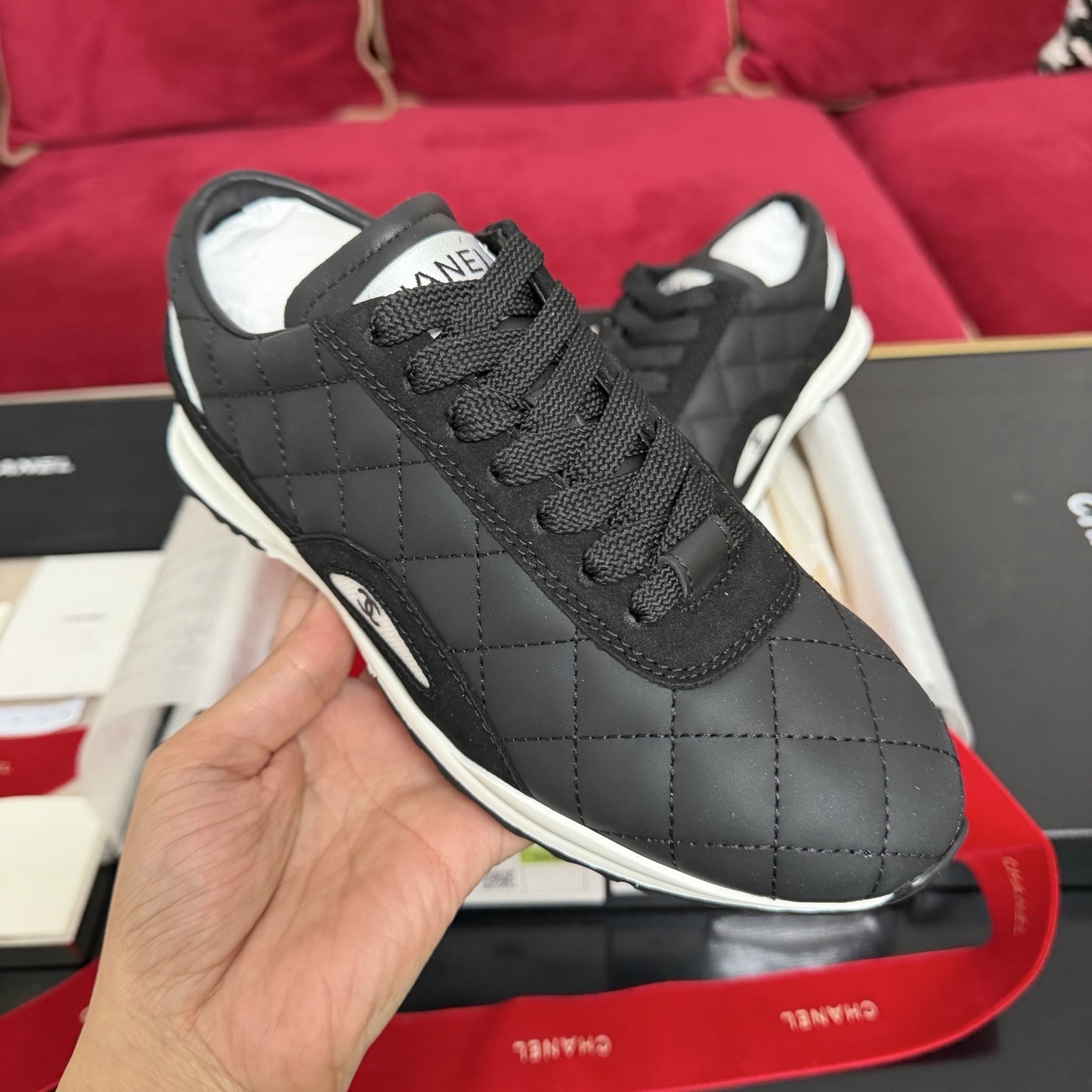 A pair of Chanel black quilted leather sneakers with white soles presented in luxury packaging with red ribbons - Hình 4