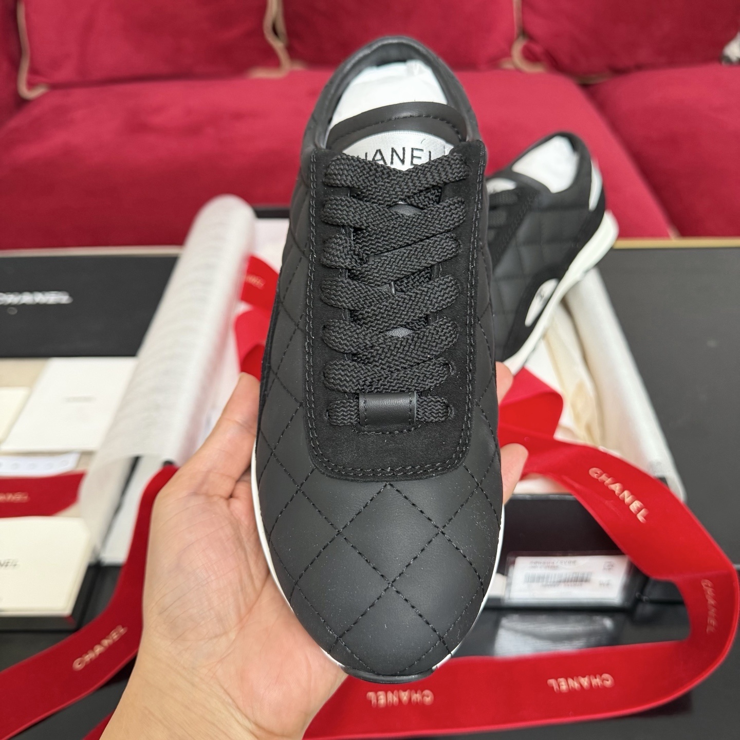 A pair of Chanel black quilted leather sneakers with white soles presented in luxury packaging with red ribbons - Hình 3