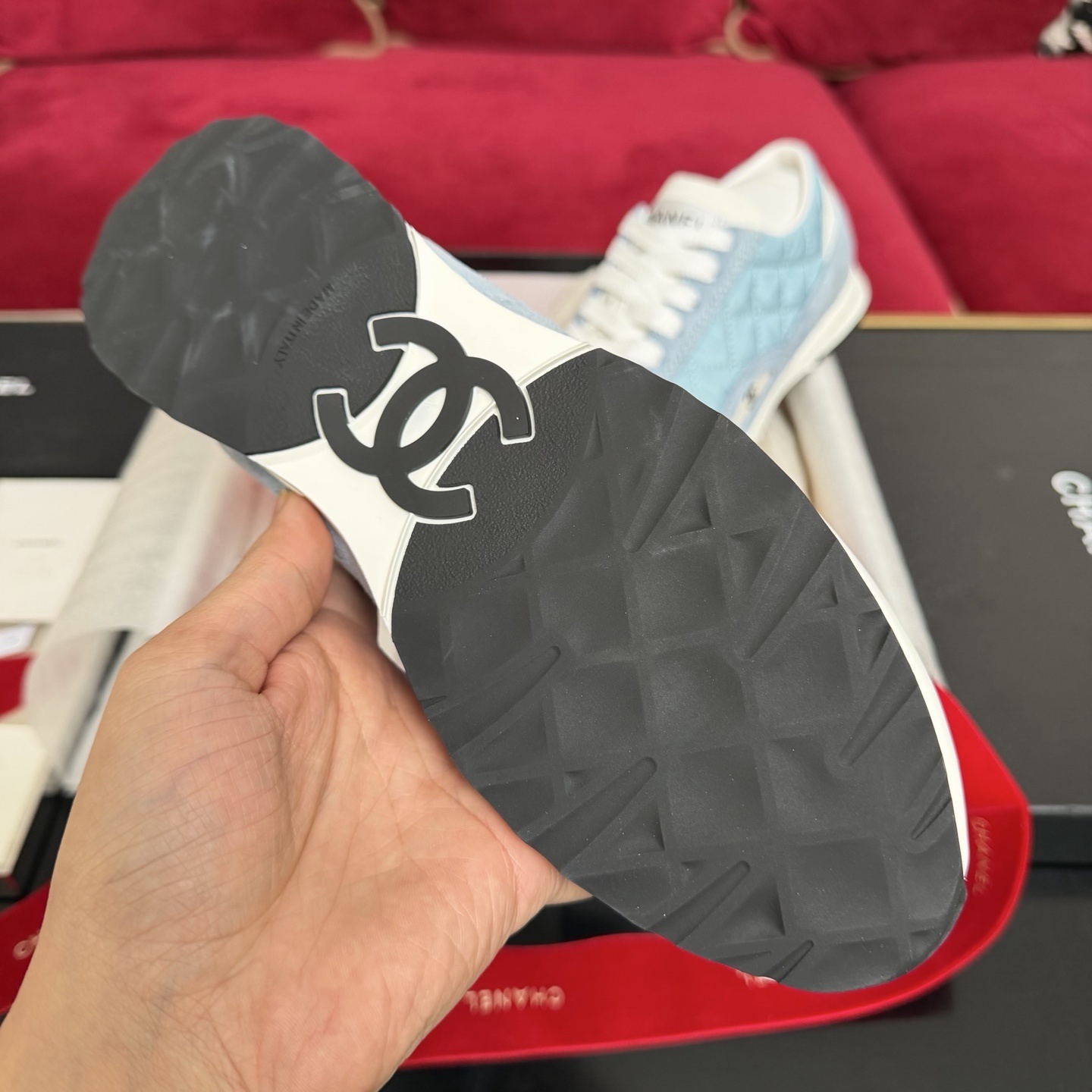 A pair of light blue quilted Chanel sneakers displayed with a black box, red ribbon, and authenticity cards. - Hình 9