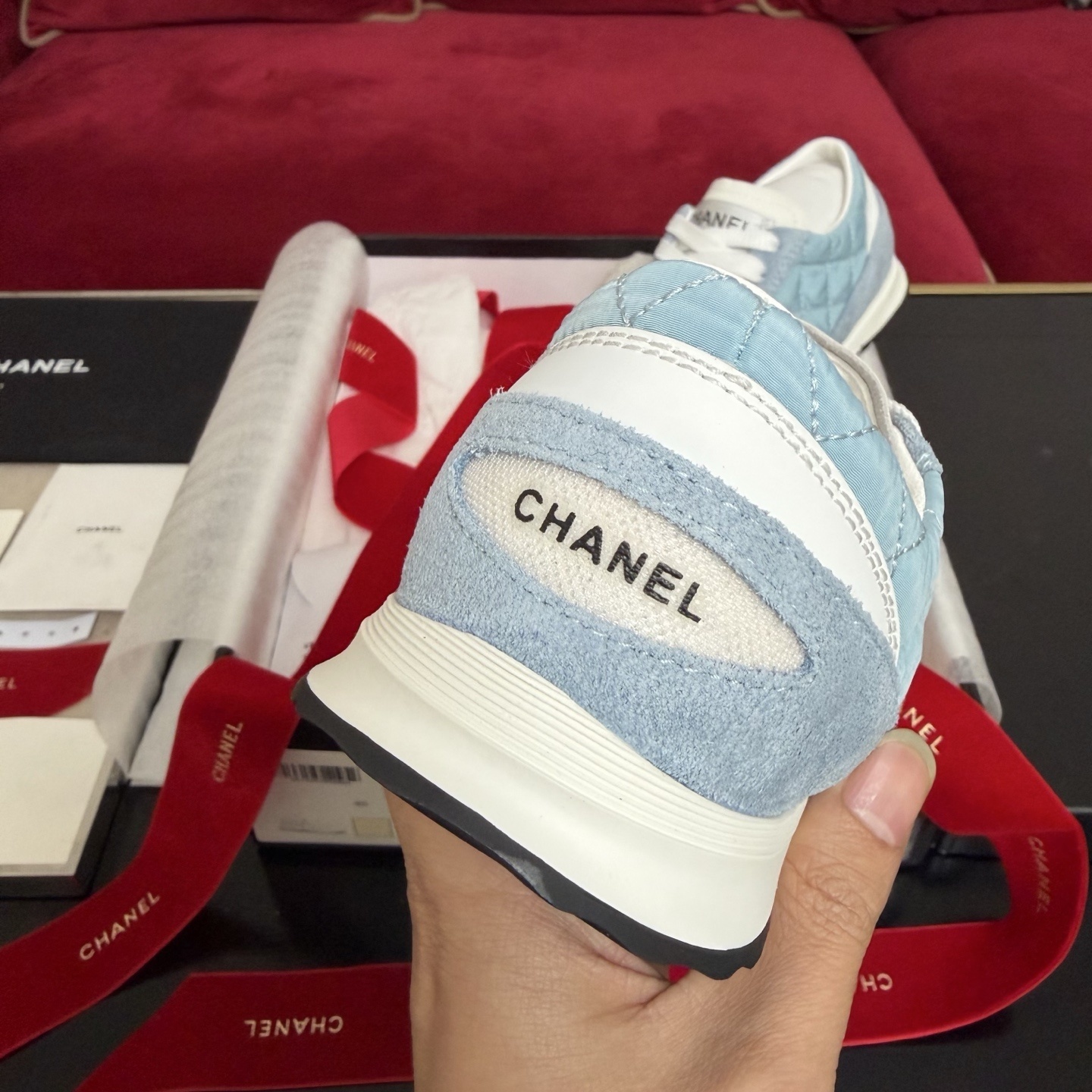 A pair of light blue quilted Chanel sneakers displayed with a black box, red ribbon, and authenticity cards. - Hình 8
