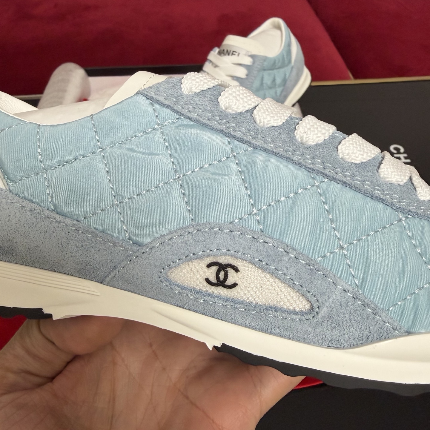 A pair of light blue quilted Chanel sneakers displayed with a black box, red ribbon, and authenticity cards. - Hình 7