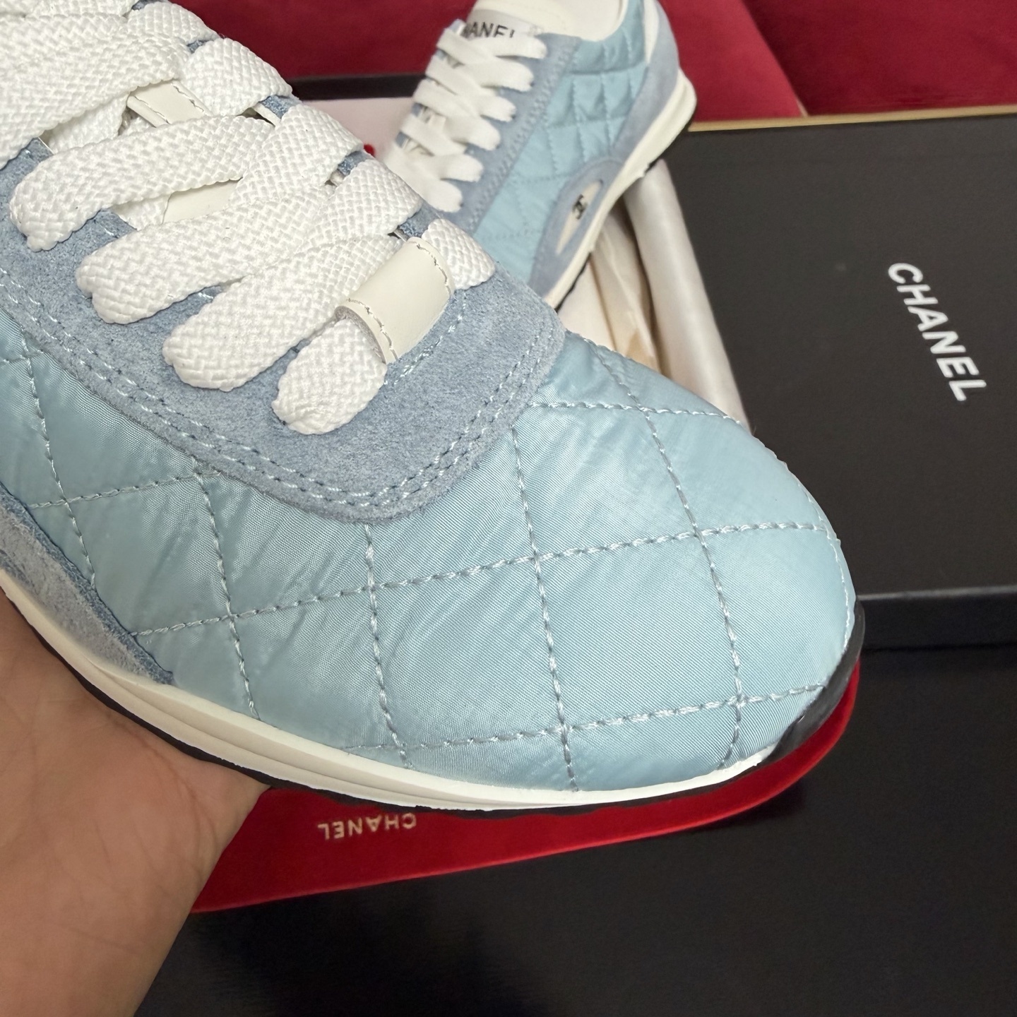 A pair of light blue quilted Chanel sneakers displayed with a black box, red ribbon, and authenticity cards. - Hình 6
