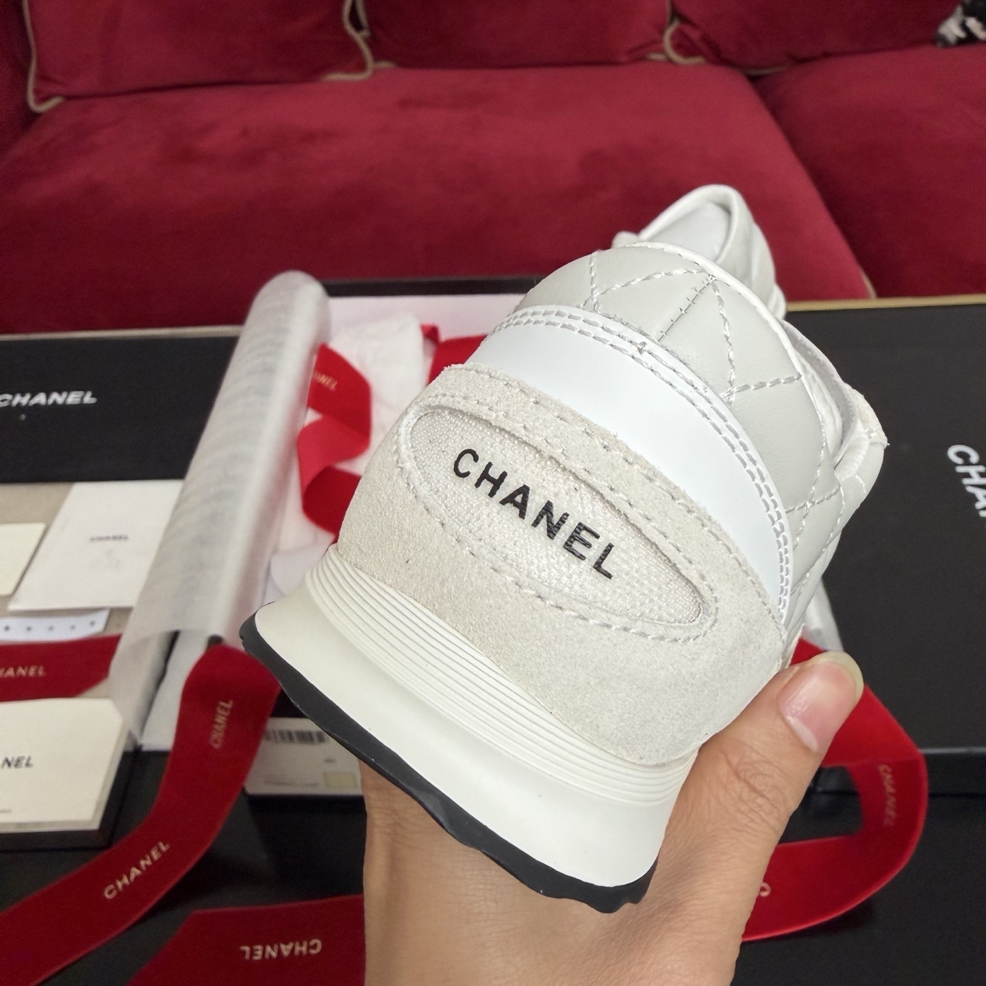 A pair of luxury white Chanel quilted leather sneakers displayed with original black box and decorative red ribbons. - Hình 8