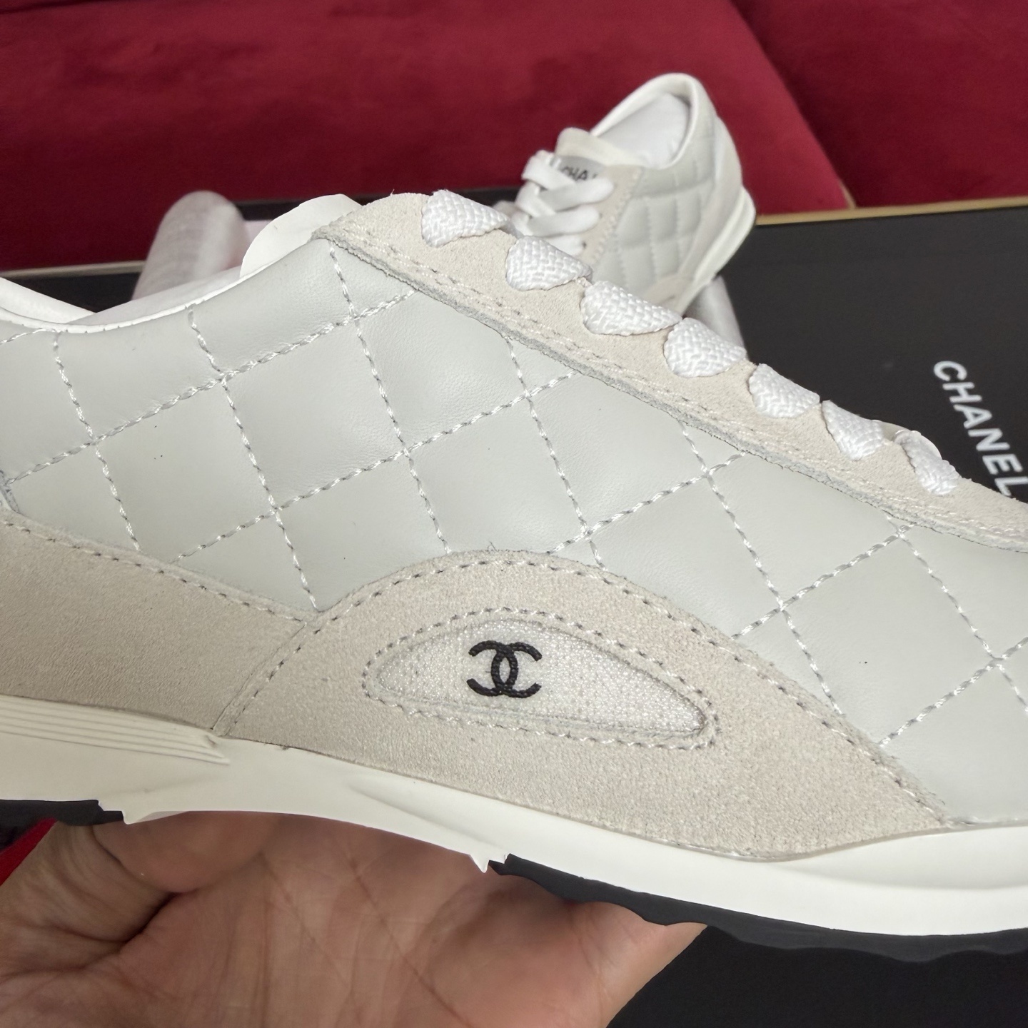 A pair of luxury white Chanel quilted leather sneakers displayed with original black box and decorative red ribbons. - Hình 7