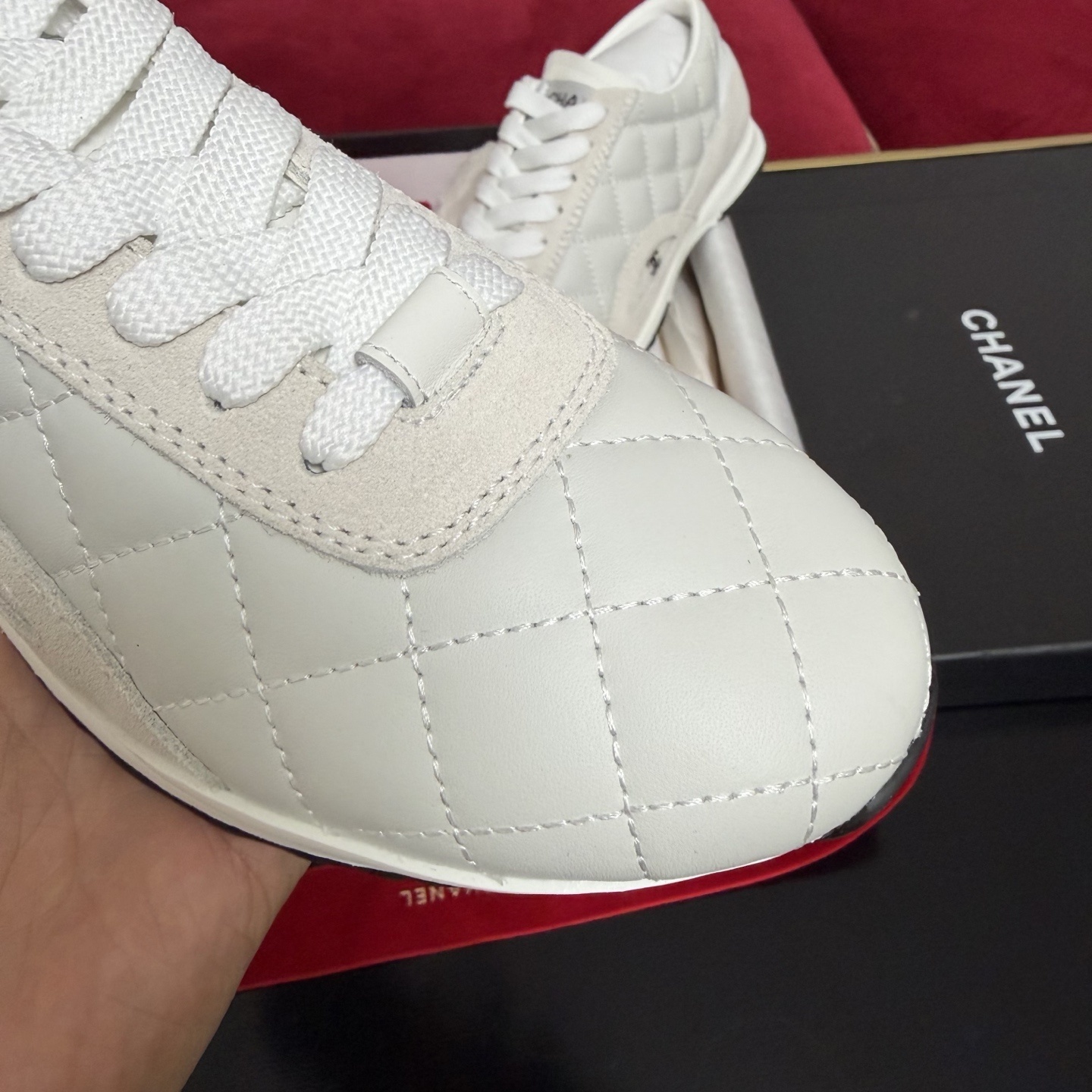 A pair of luxury white Chanel quilted leather sneakers displayed with original black box and decorative red ribbons. - Hình 6