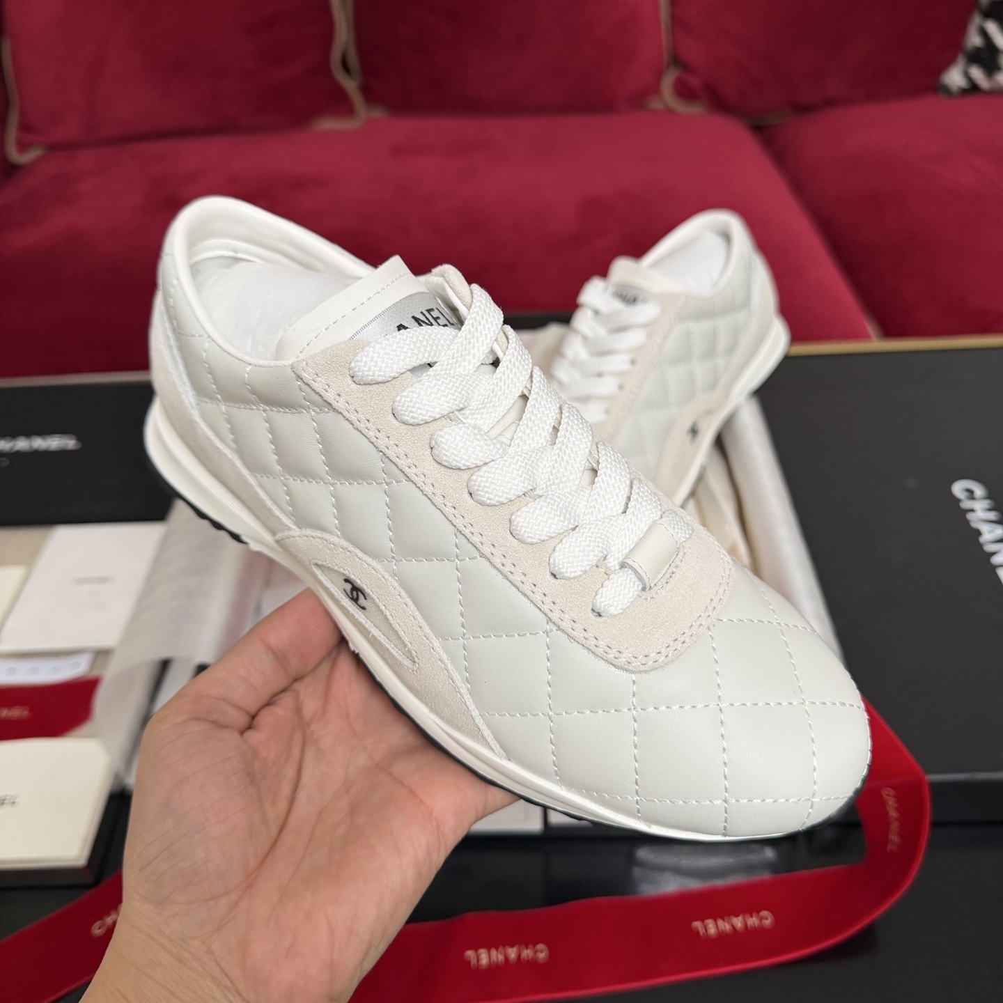 A pair of luxury white Chanel quilted leather sneakers displayed with original black box and decorative red ribbons. - Hình 4