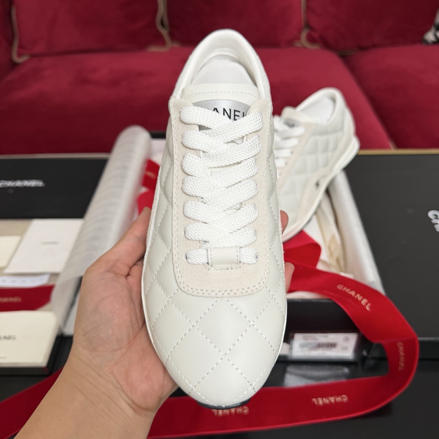 A pair of luxury white Chanel quilted leather sneakers displayed with original black box and decorative red ribbons. - Hình 3