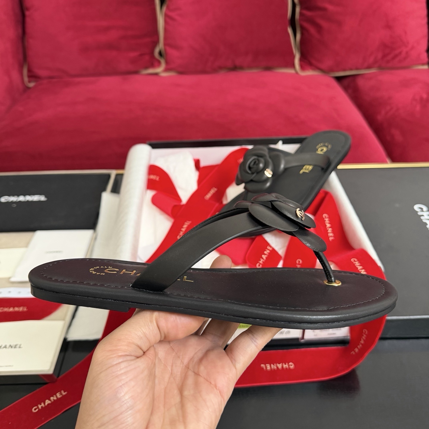 Black Chanel leather thong sandals with 3D Camellia flower and gold CC logo in a luxury gift box with red ribbons. - Hình 5