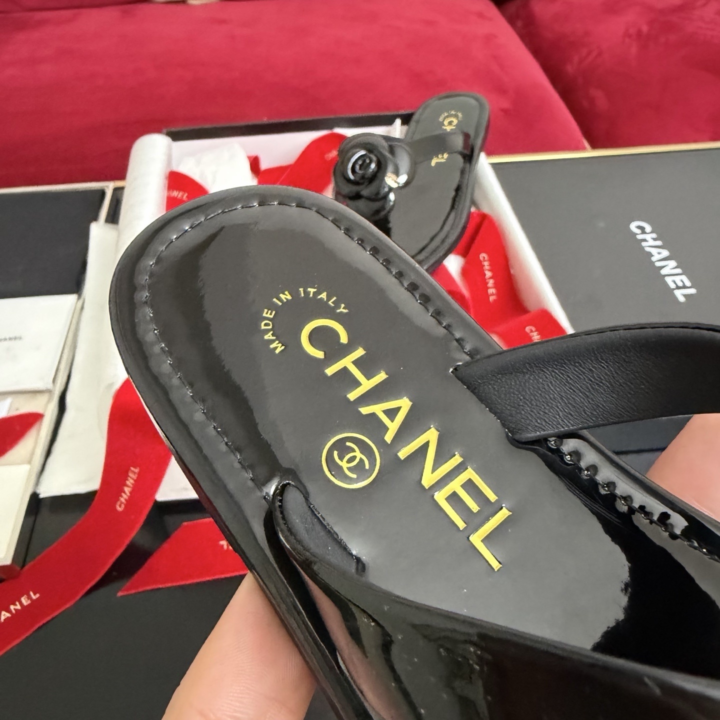 Pair of black Chanel patent leather thong sandals featuring a large camellia flower and gold CC logo, displayed in original luxury packaging. - Hình 7