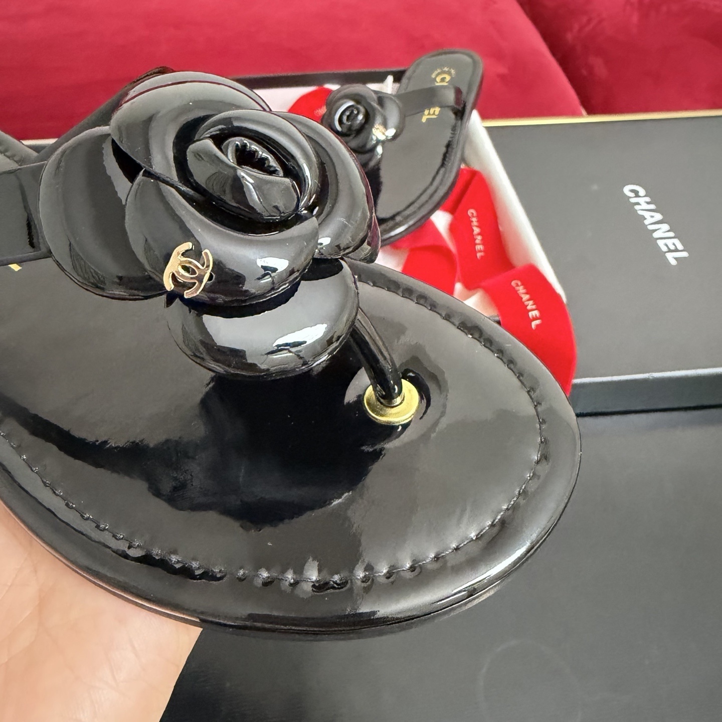 Pair of black Chanel patent leather thong sandals featuring a large camellia flower and gold CC logo, displayed in original luxury packaging. - Hình 6