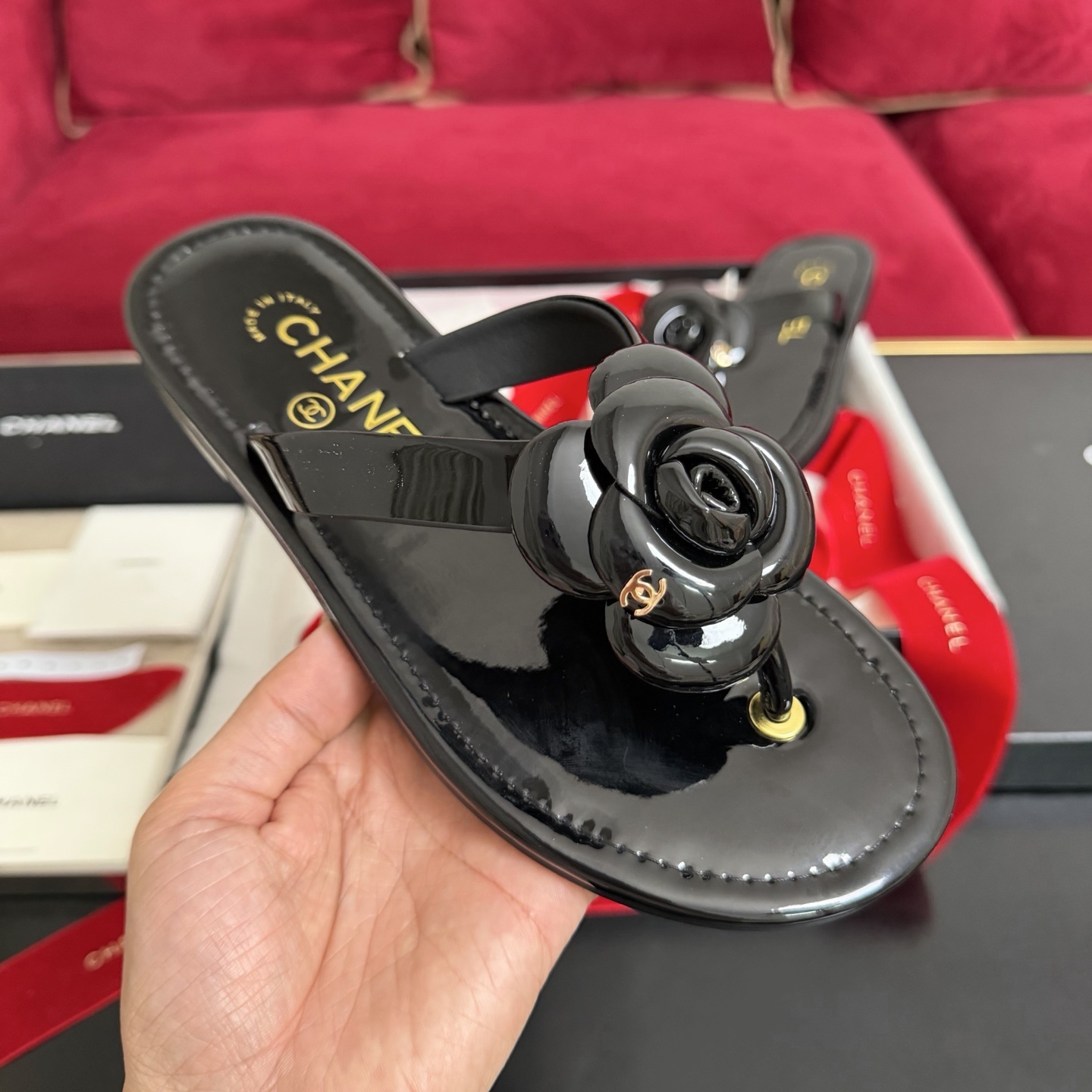 Pair of black Chanel patent leather thong sandals featuring a large camellia flower and gold CC logo, displayed in original luxury packaging. - Hình 4