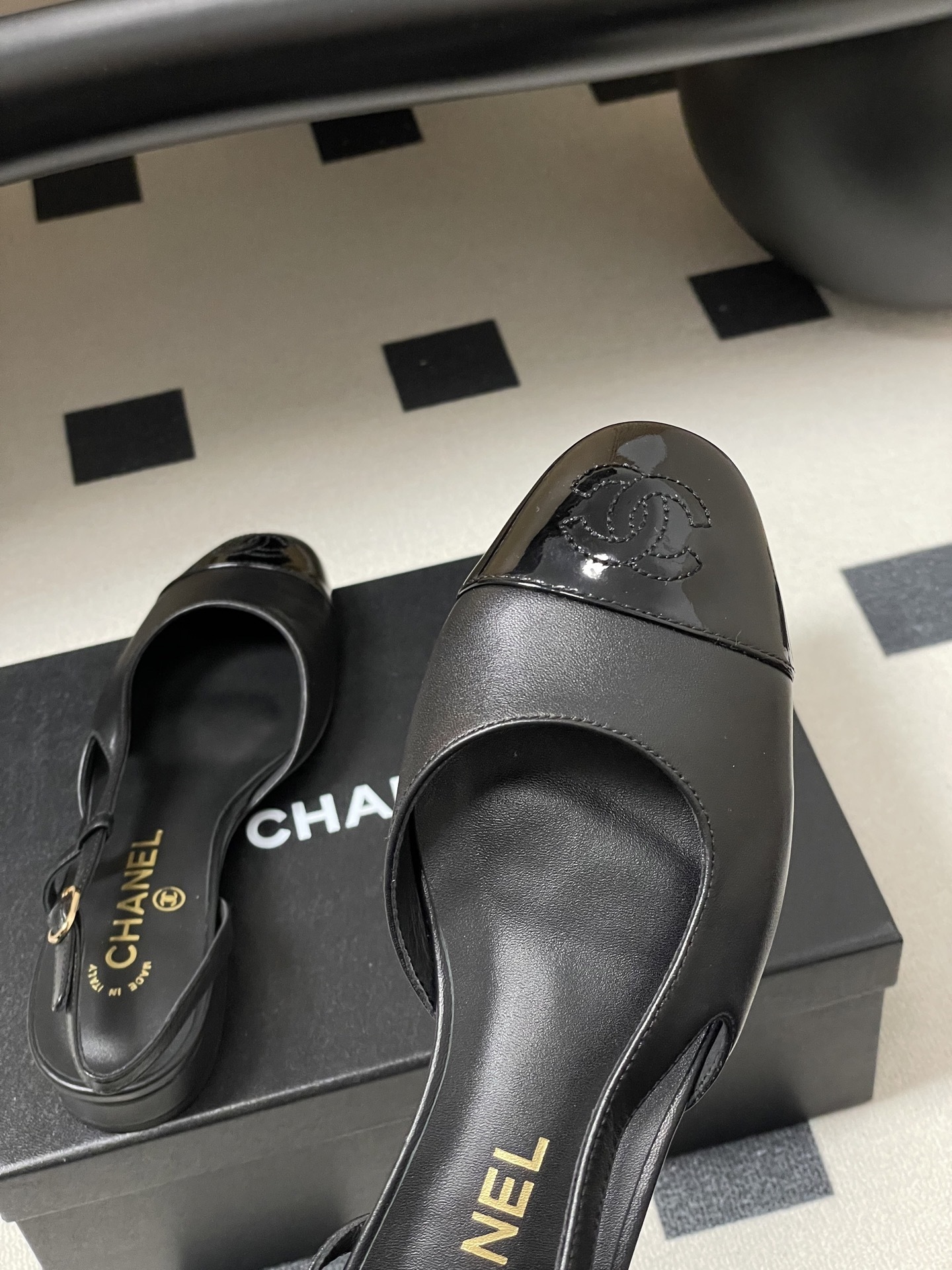 Pair of Chanel black leather slingback pumps with patent cap toe and gold CC logo on a black surface - Hình 9