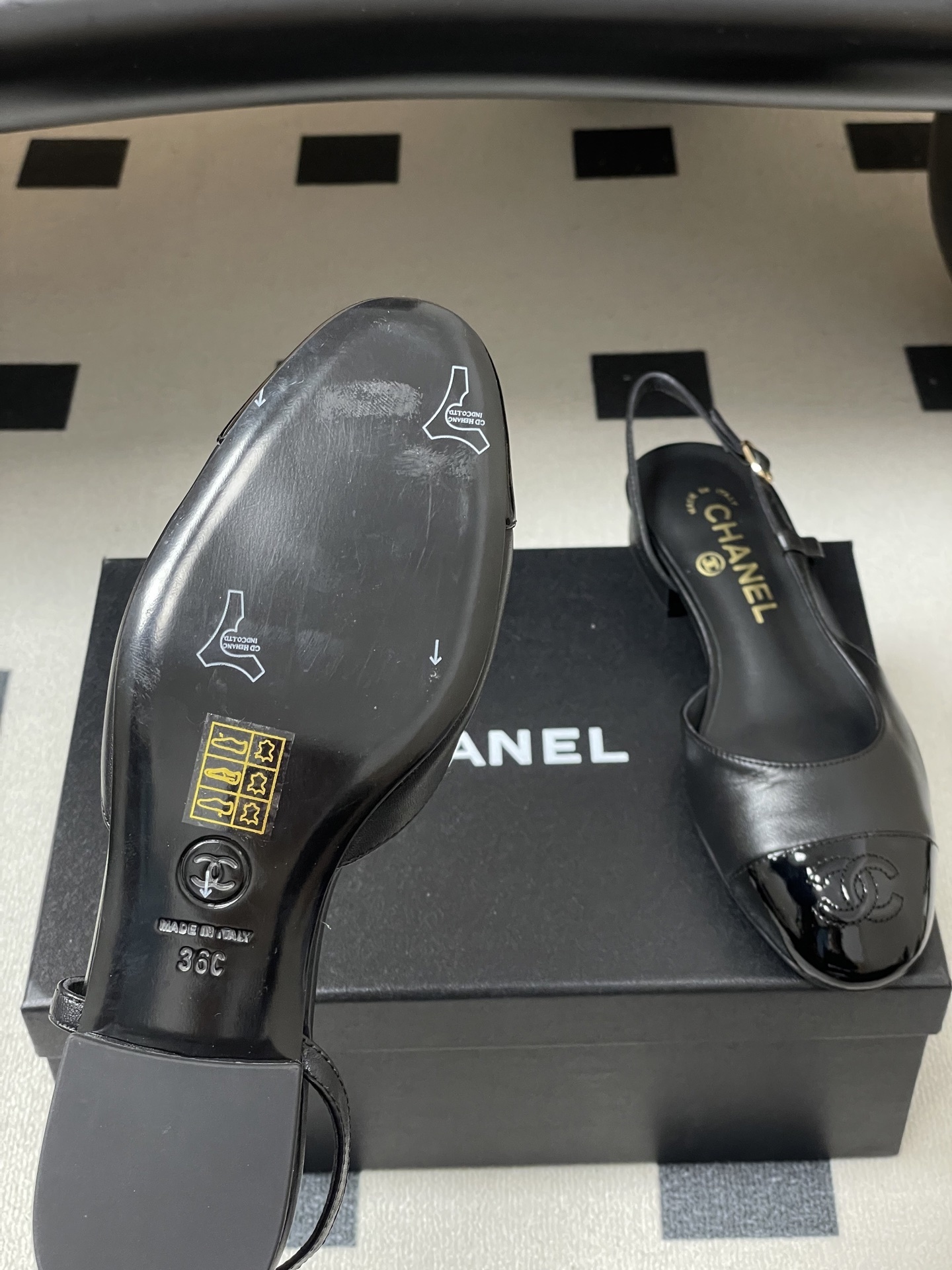 Pair of Chanel black leather slingback pumps with patent cap toe and gold CC logo on a black surface - Hình 8