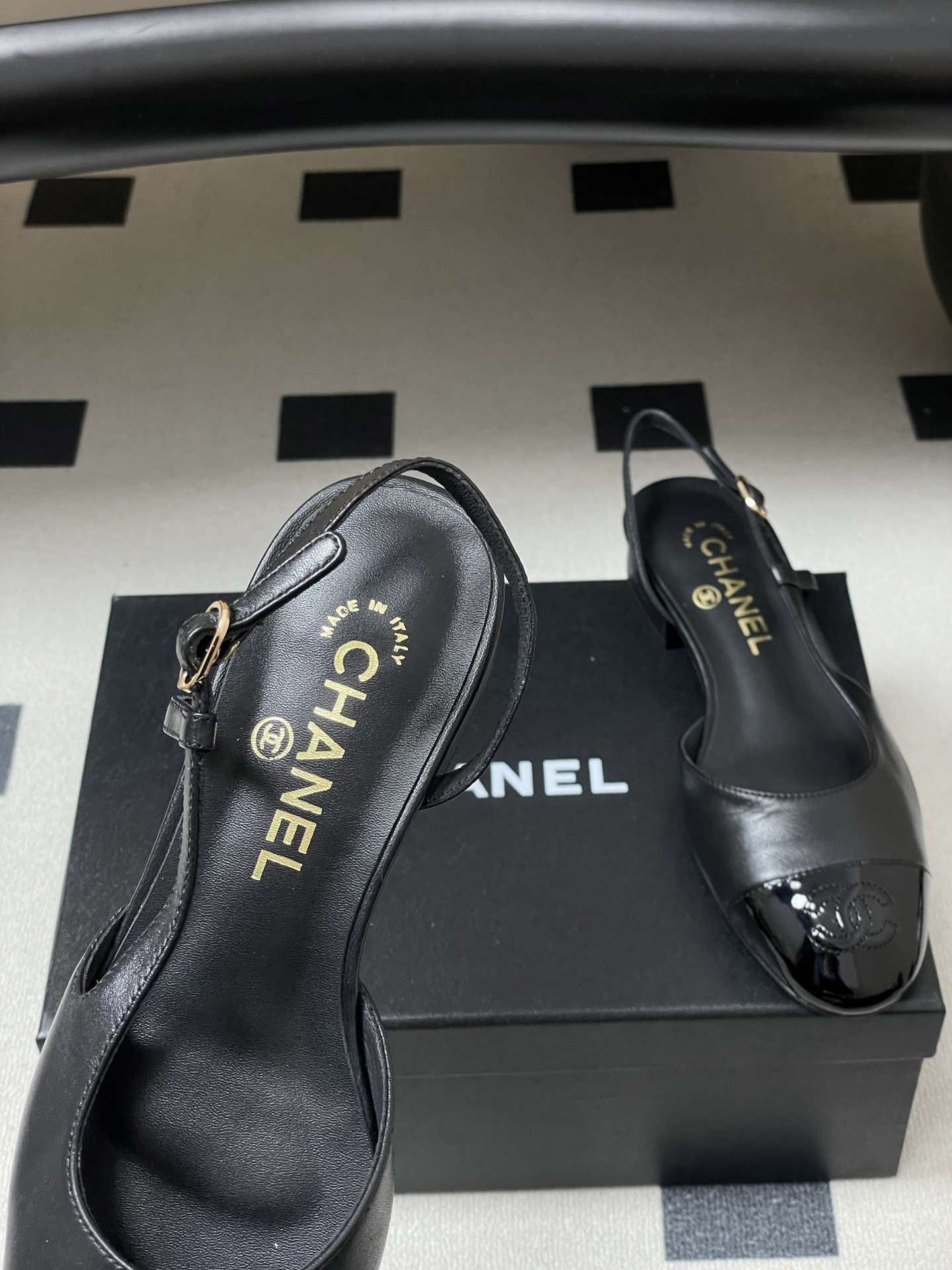 Pair of Chanel black leather slingback pumps with patent cap toe and gold CC logo on a black surface - Hình 7