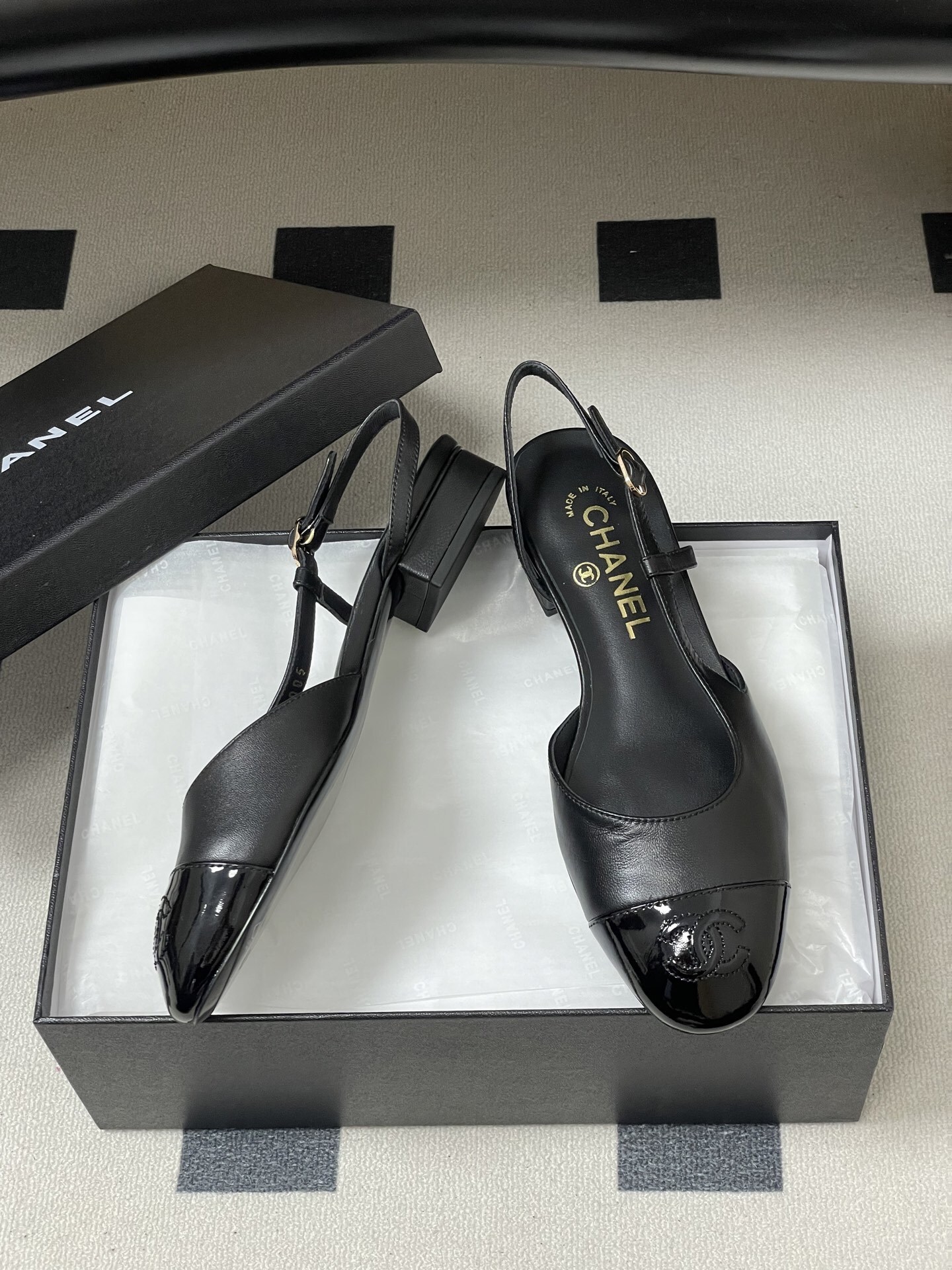 Pair of Chanel black leather slingback pumps with patent cap toe and gold CC logo on a black surface - Hình 6