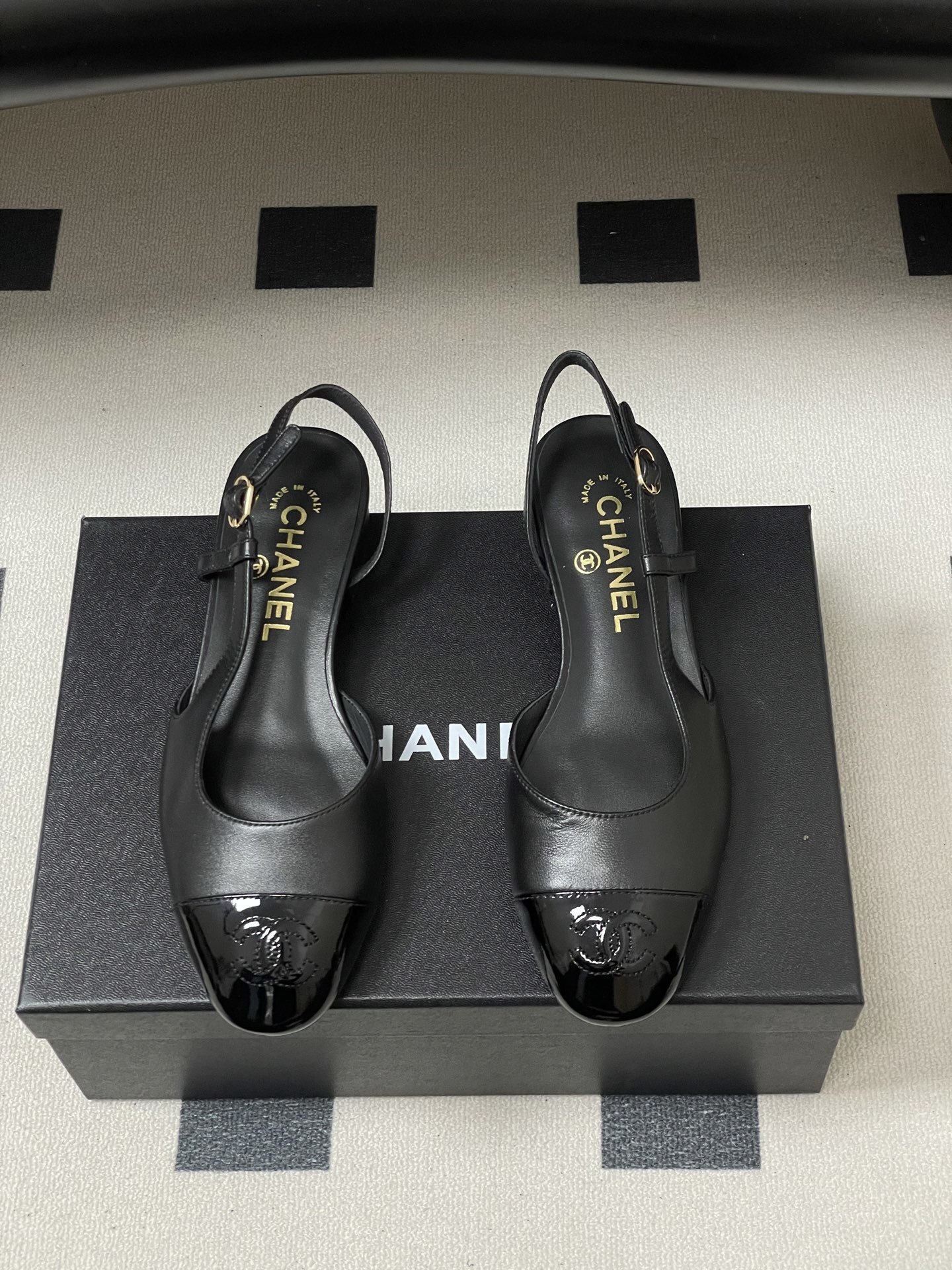 Pair of Chanel black leather slingback pumps with patent cap toe and gold CC logo on a black surface - Hình 5