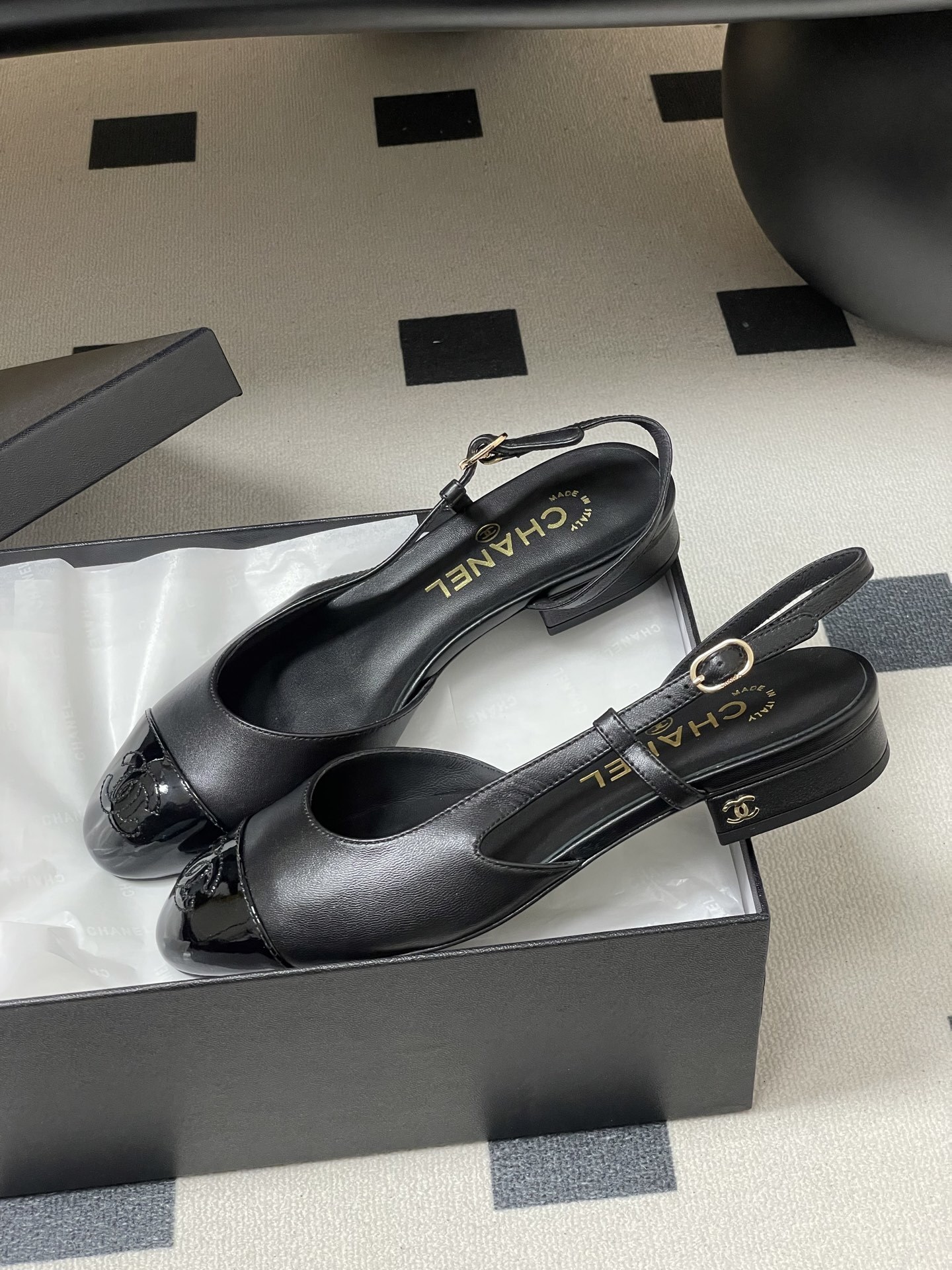 Pair of Chanel black leather slingback pumps with patent cap toe and gold CC logo on a black surface - Hình 4