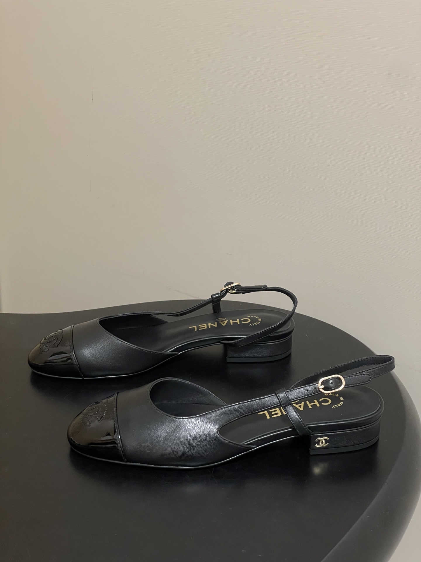 Pair of Chanel black leather slingback pumps with patent cap toe and gold CC logo on a black surface - Hình 3