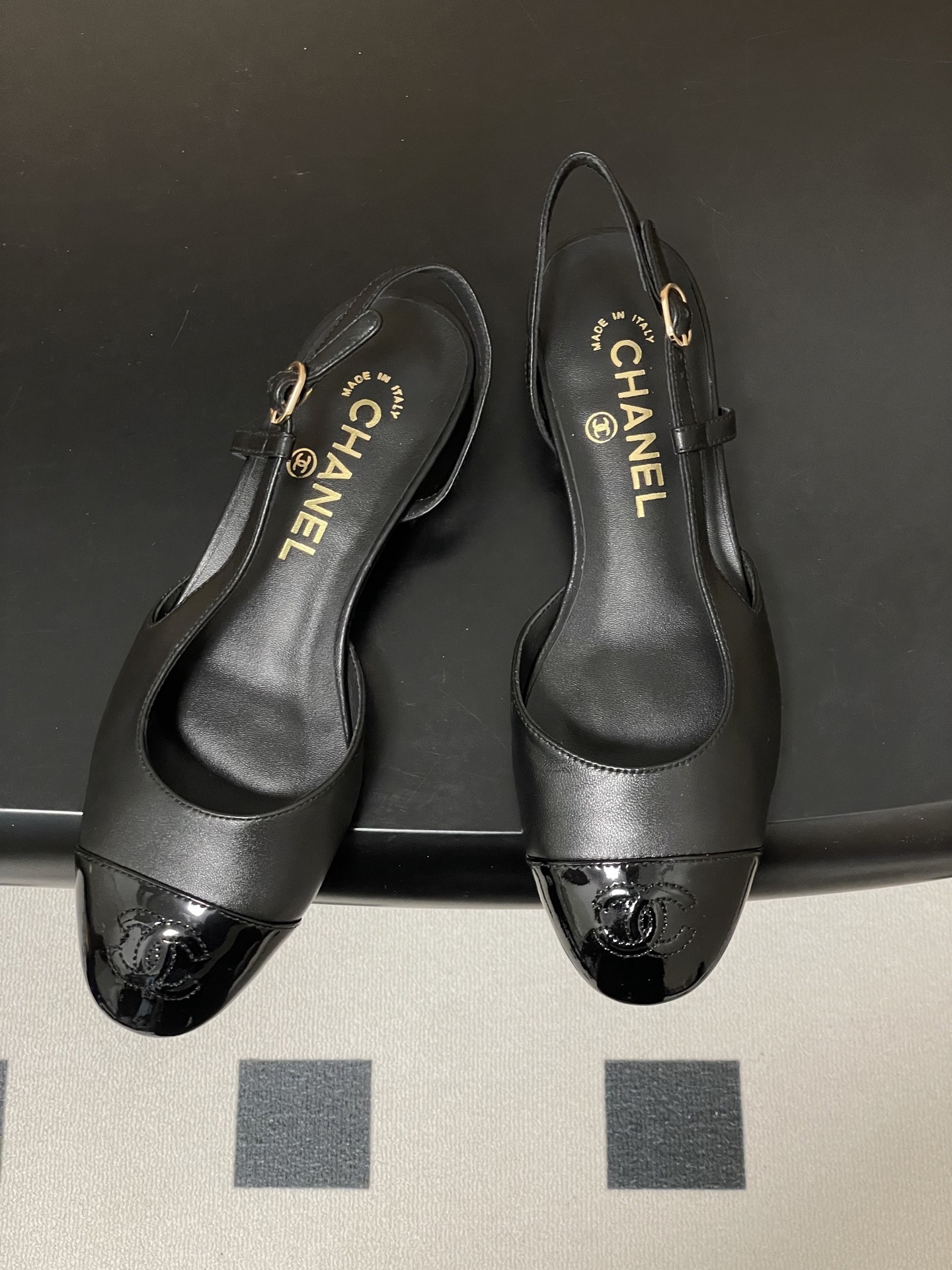 Pair of Chanel black leather slingback pumps with patent cap toe and gold CC logo on a black surface - Hình 2