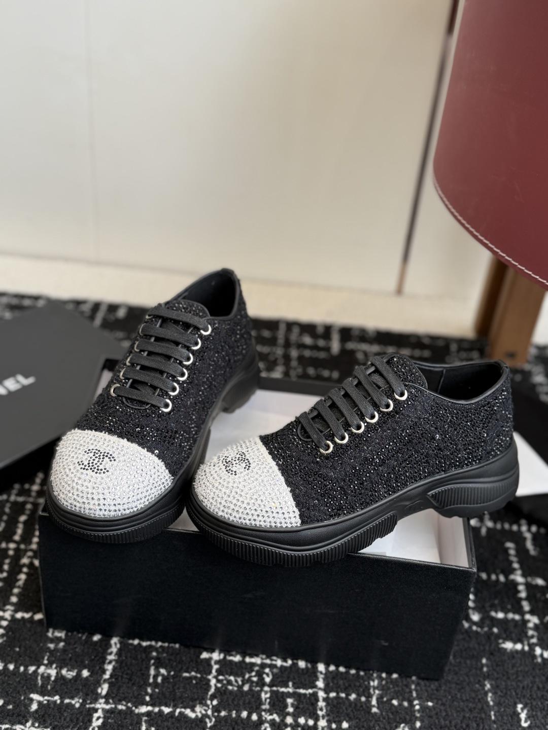 A pair of luxury Chanel black and white sneakers covered in sparkling crystals with a black CC logo on the toe cap. - Hình 3