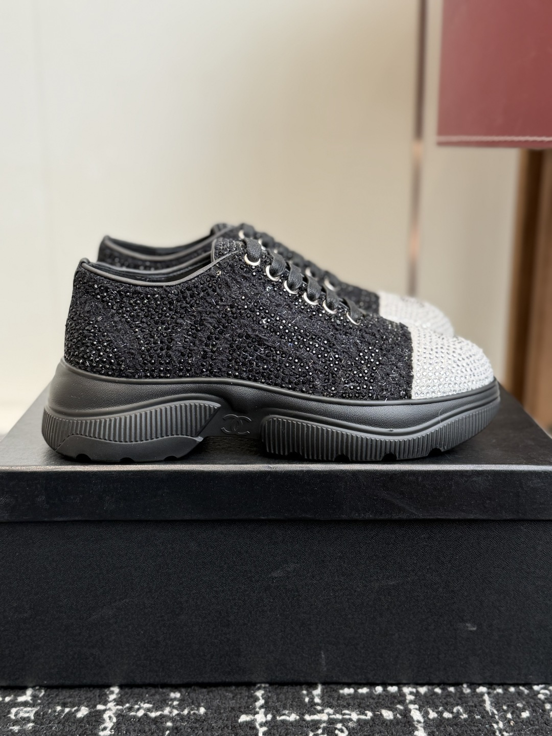 A pair of luxury Chanel black and white sneakers covered in sparkling crystals with a black CC logo on the toe cap. - Hình 2