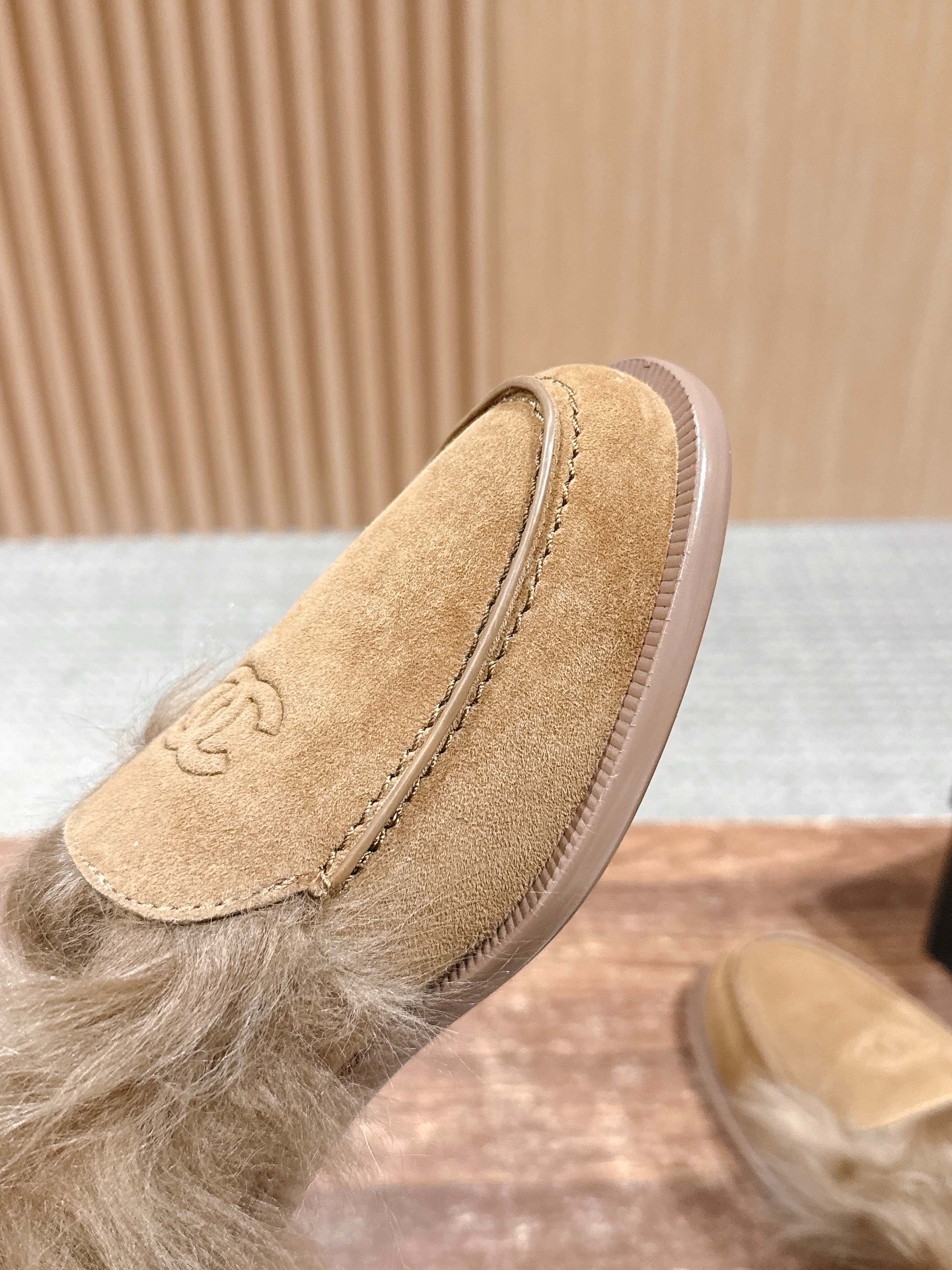 A pair of tan Chanel suede loafers with fluffy brown fur trim and embossed CC logo on a wooden surface next to a black shoe box. - Hình 6
