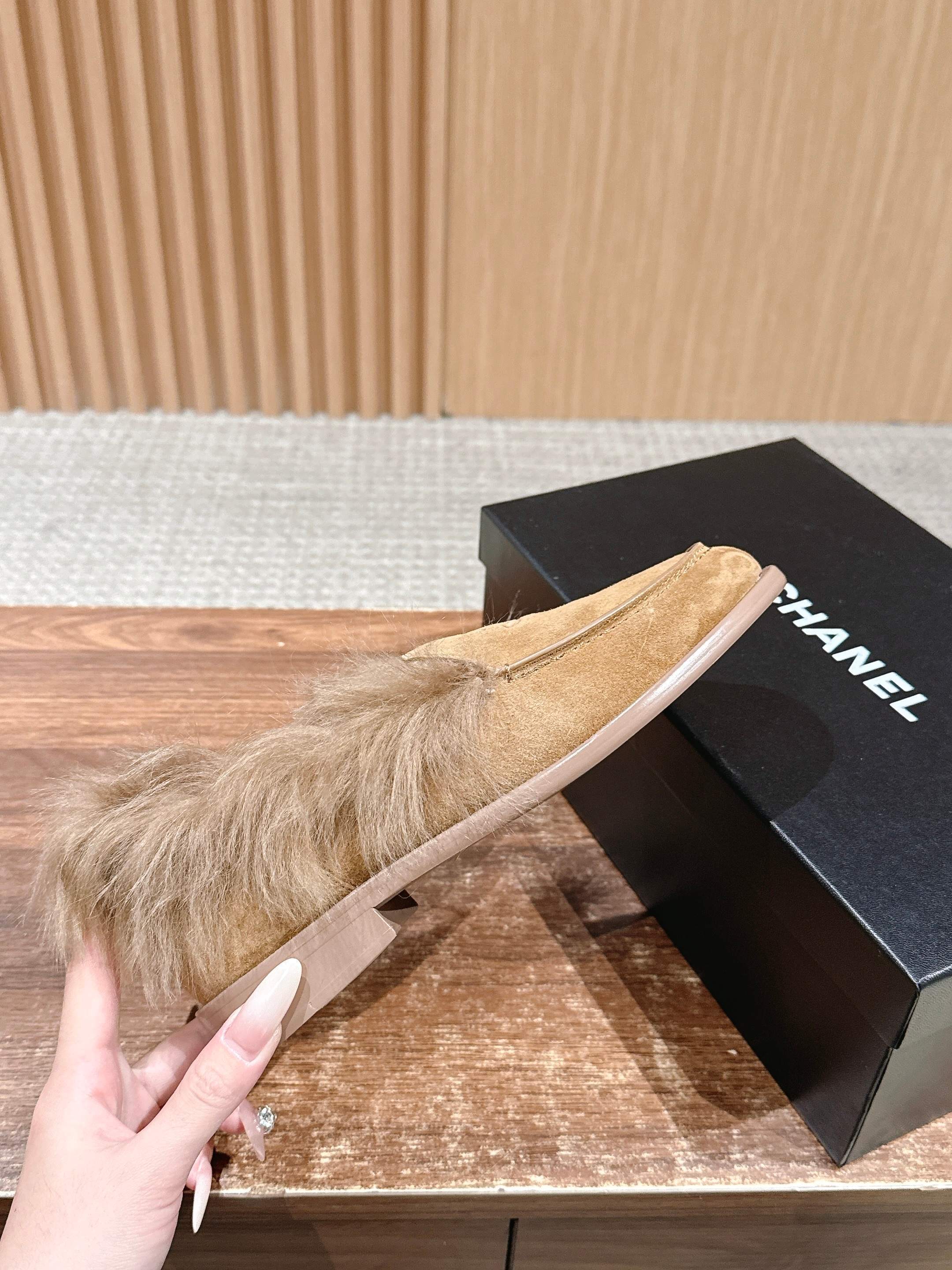 A pair of tan Chanel suede loafers with fluffy brown fur trim and embossed CC logo on a wooden surface next to a black shoe box. - Hình 5
