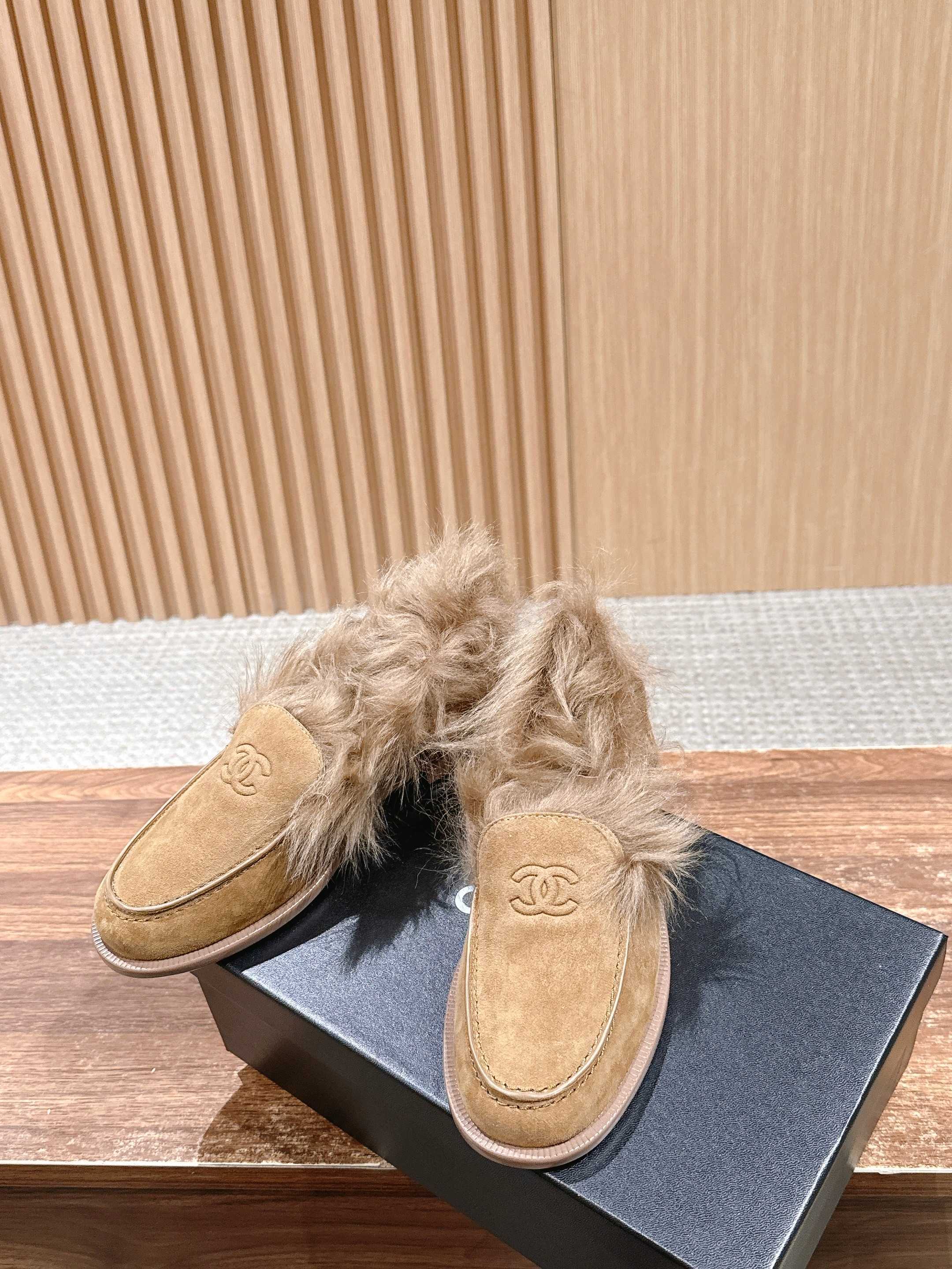 A pair of tan Chanel suede loafers with fluffy brown fur trim and embossed CC logo on a wooden surface next to a black shoe box. - Hình 4
