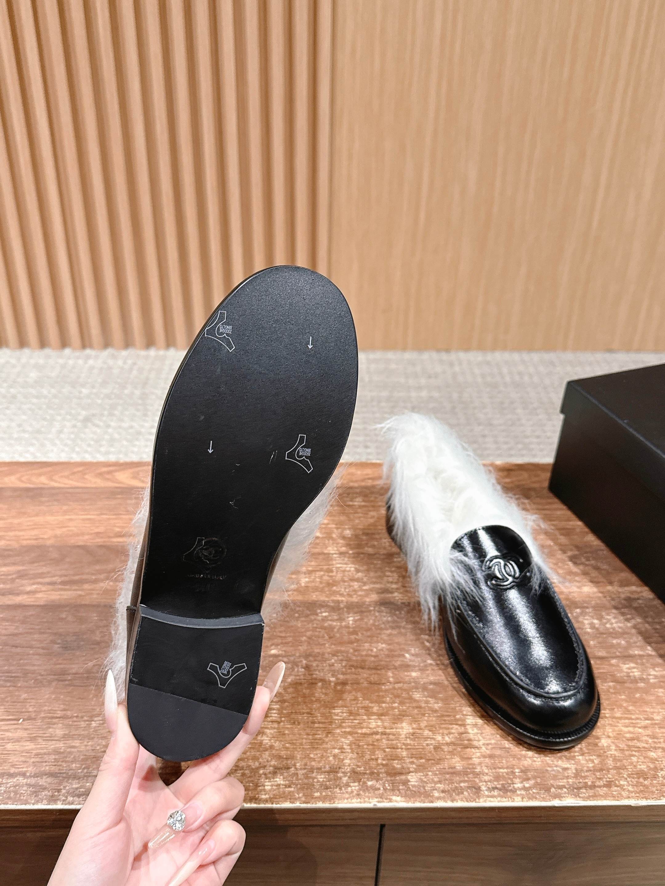 A pair of luxury black leather Chanel loafers with prominent white fur lining and CC logo on a wooden surface. - Hình 9
