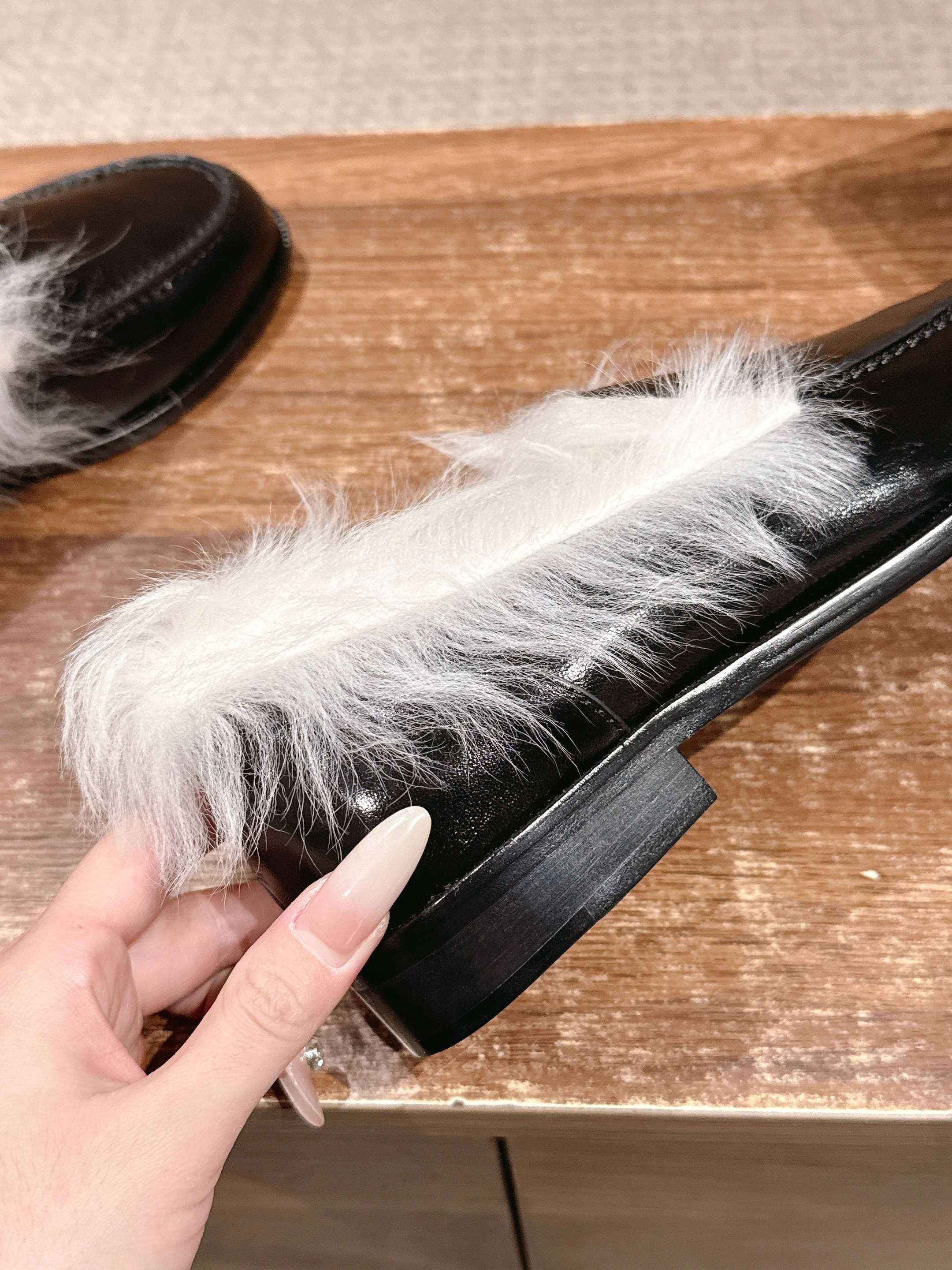 A pair of luxury black leather Chanel loafers with prominent white fur lining and CC logo on a wooden surface. - Hình 8