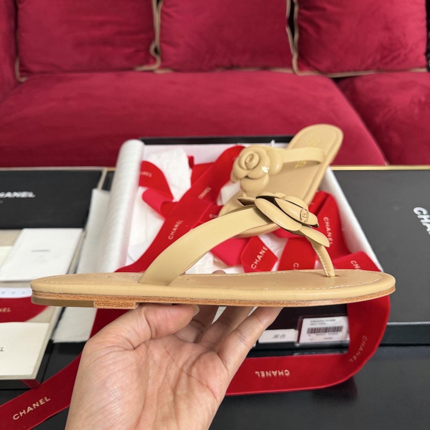 Pair of beige Chanel leather thong sandals featuring a large 3D camellia flower and gold CC logo detail, shown with original luxury packaging. - Hình 5
