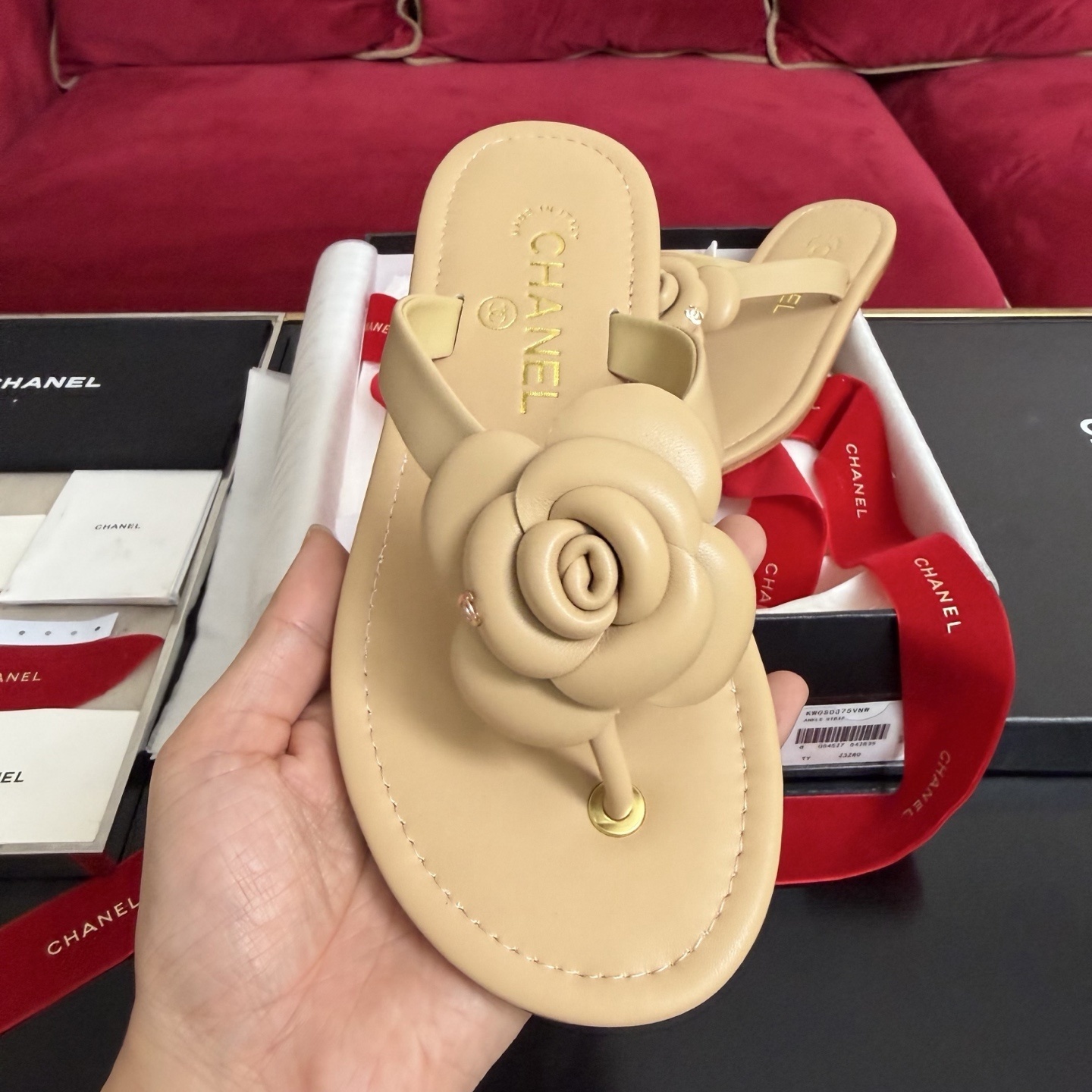 Pair of beige Chanel leather thong sandals featuring a large 3D camellia flower and gold CC logo detail, shown with original luxury packaging. - Hình 3