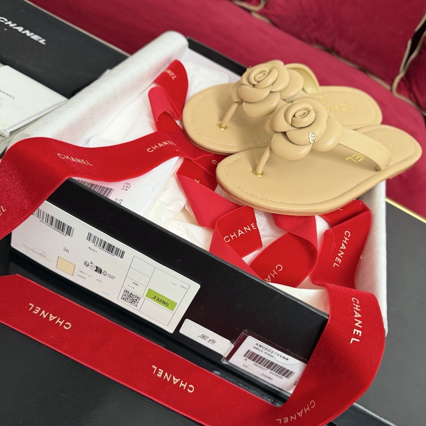 Pair of beige Chanel leather thong sandals featuring a large 3D camellia flower and gold CC logo detail, shown with original luxury packaging. - Hình 2