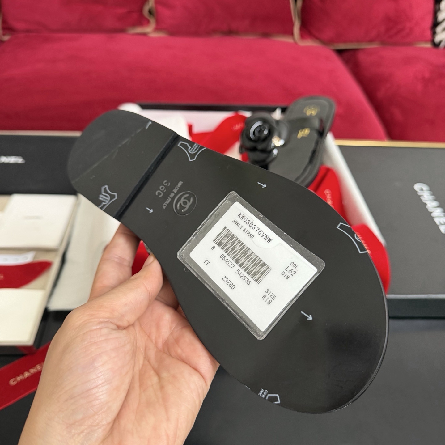 Authentic black Chanel thong sandals featuring a large 3D Camellia flower with a small gold CC logo, presented in a gift box with a red Chanel ribbon. - Hình 9