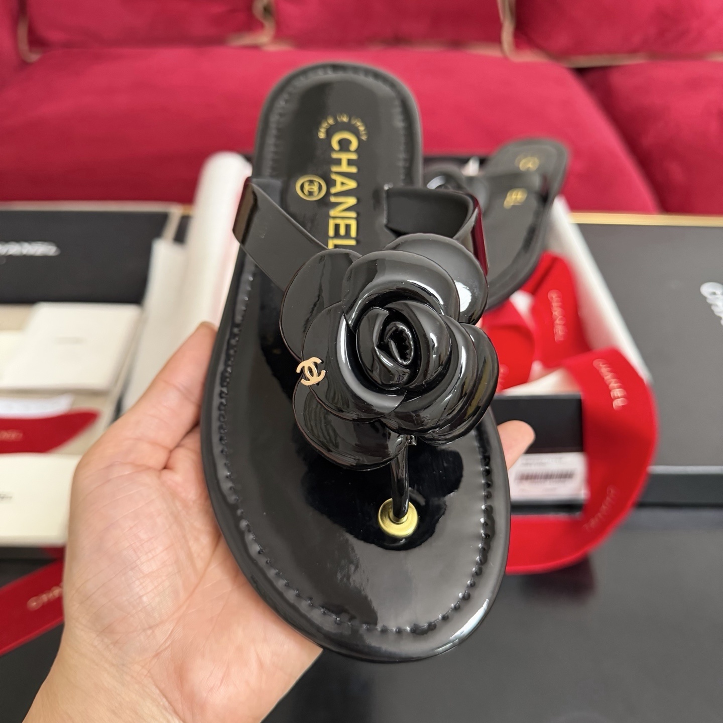 Authentic black Chanel thong sandals featuring a large 3D Camellia flower with a small gold CC logo, presented in a gift box with a red Chanel ribbon. - Hình 3
