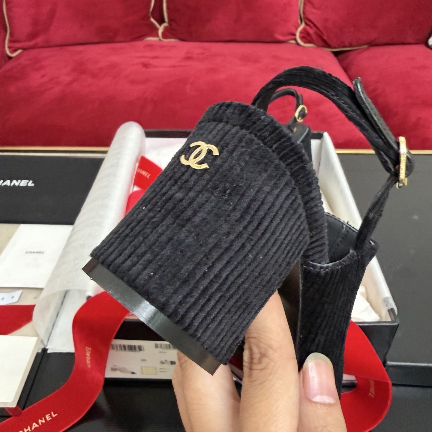 A pair of black Chanel ribbed fabric slingback pumps with a CC logo on the cap toe, displayed in their original box with a red ribbon. - Hình 8