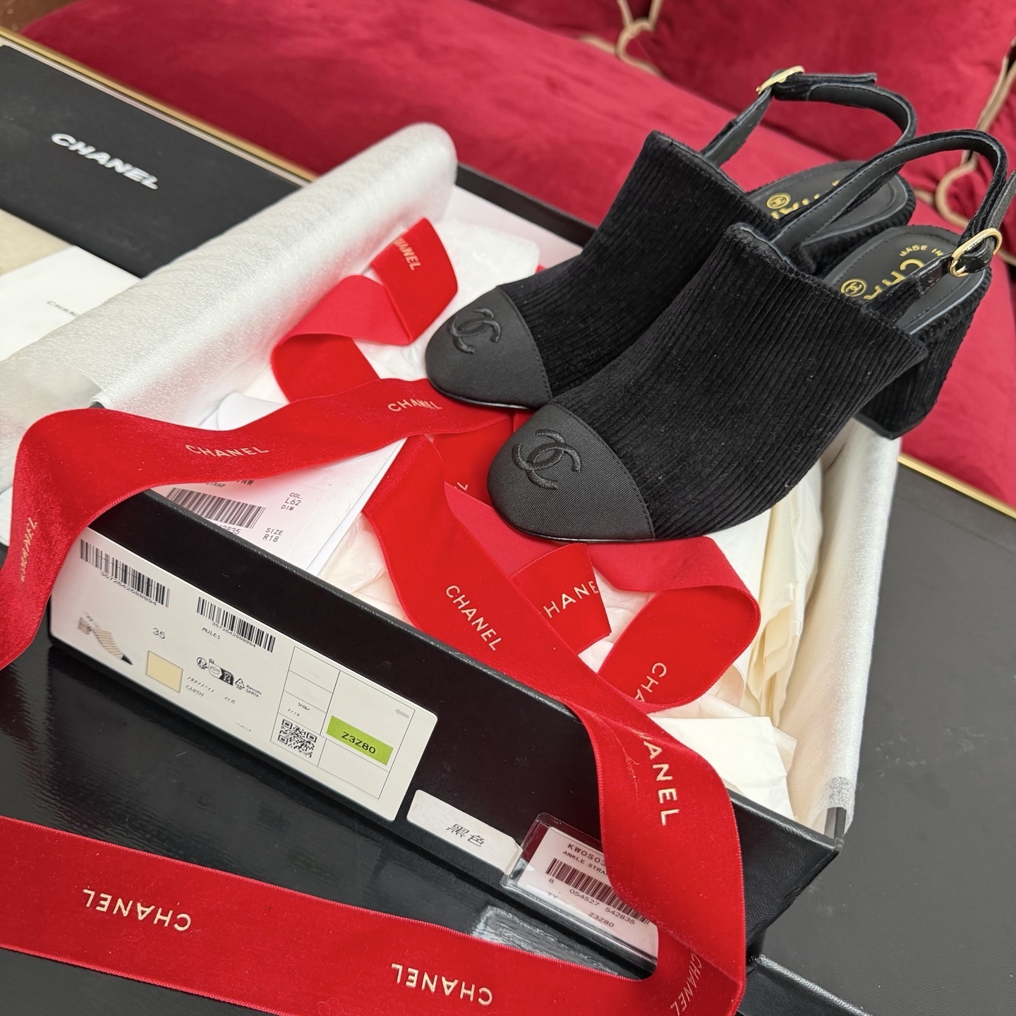 A pair of black Chanel ribbed fabric slingback pumps with a CC logo on the cap toe, displayed in their original box with a red ribbon. - Hình 2