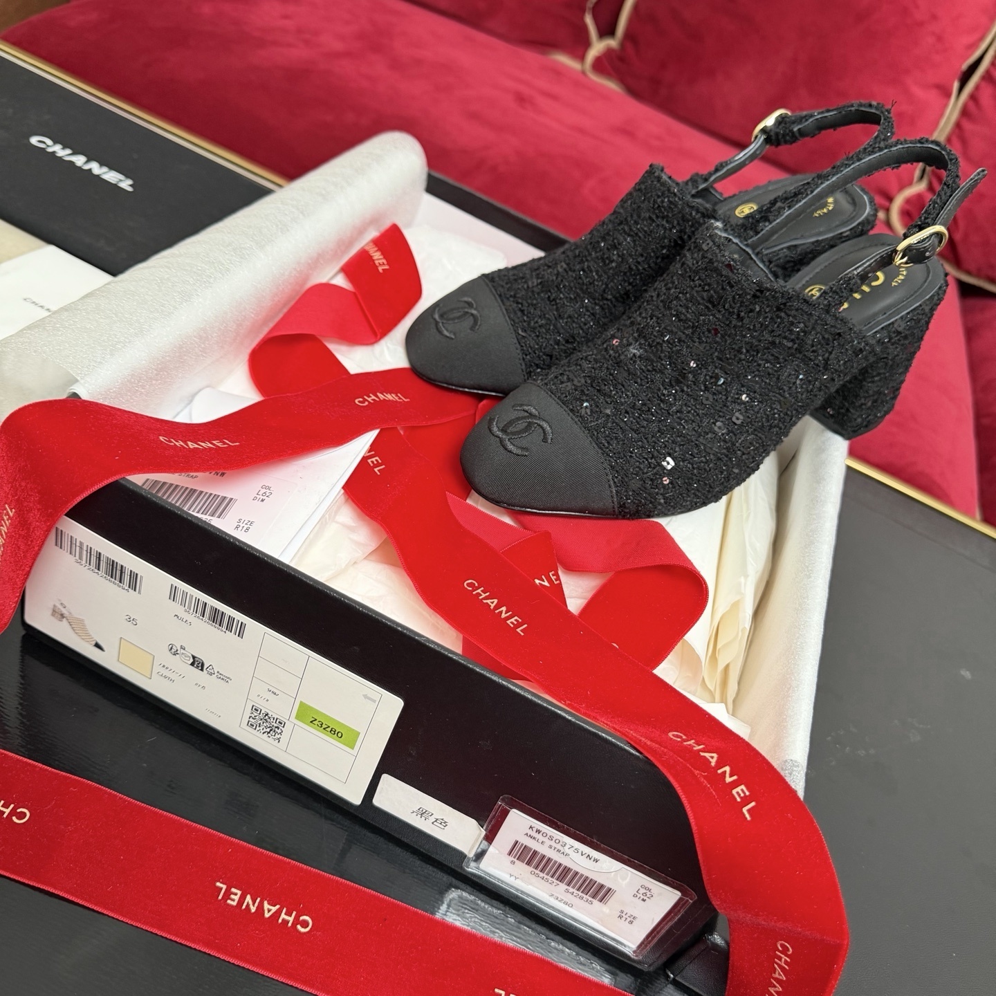 Pair of Chanel black tweed slingback pumps with sequins and CC logo on toe cap, displayed in original packaging with red ribbon. - Hình 2