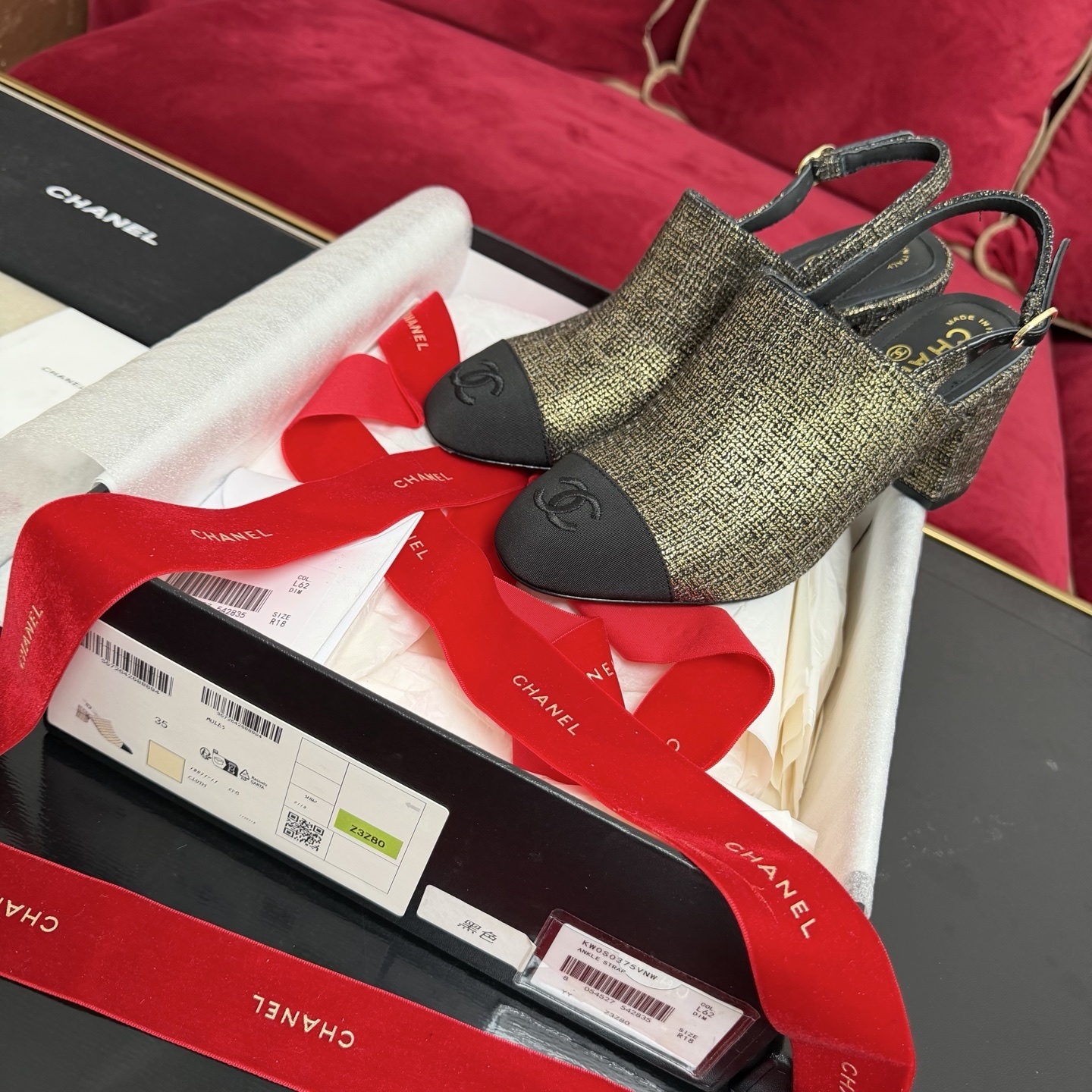 Pair of Chanel gold metallic tweed slingback pumps with black CC logo cap toe and block heel sitting in a gift box with red ribbon. - Hình 2