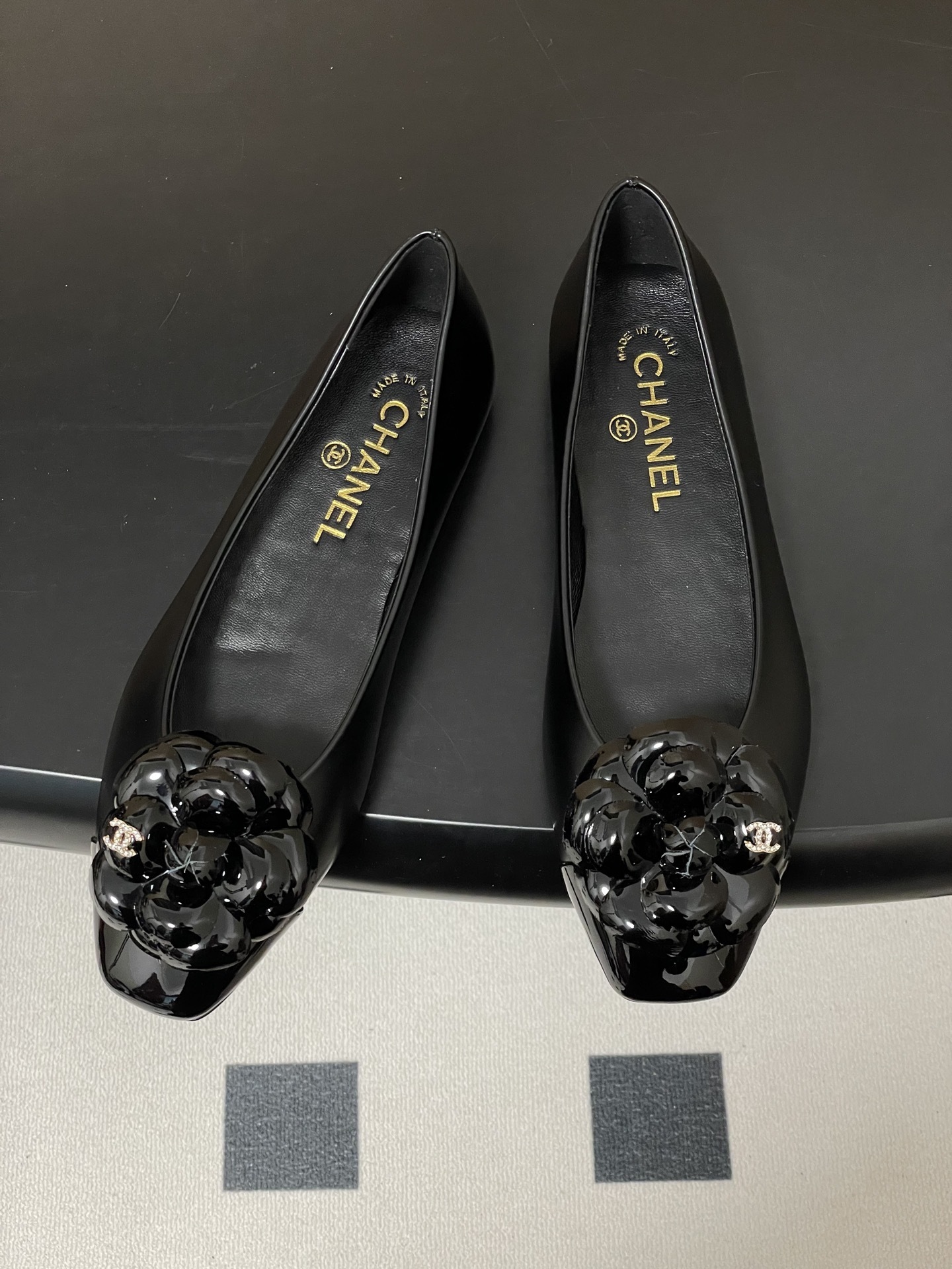 A pair of black Chanel ballet flats featuring a patent leather camellia flower with a small CC logo on the toe cap. - Hình 2
